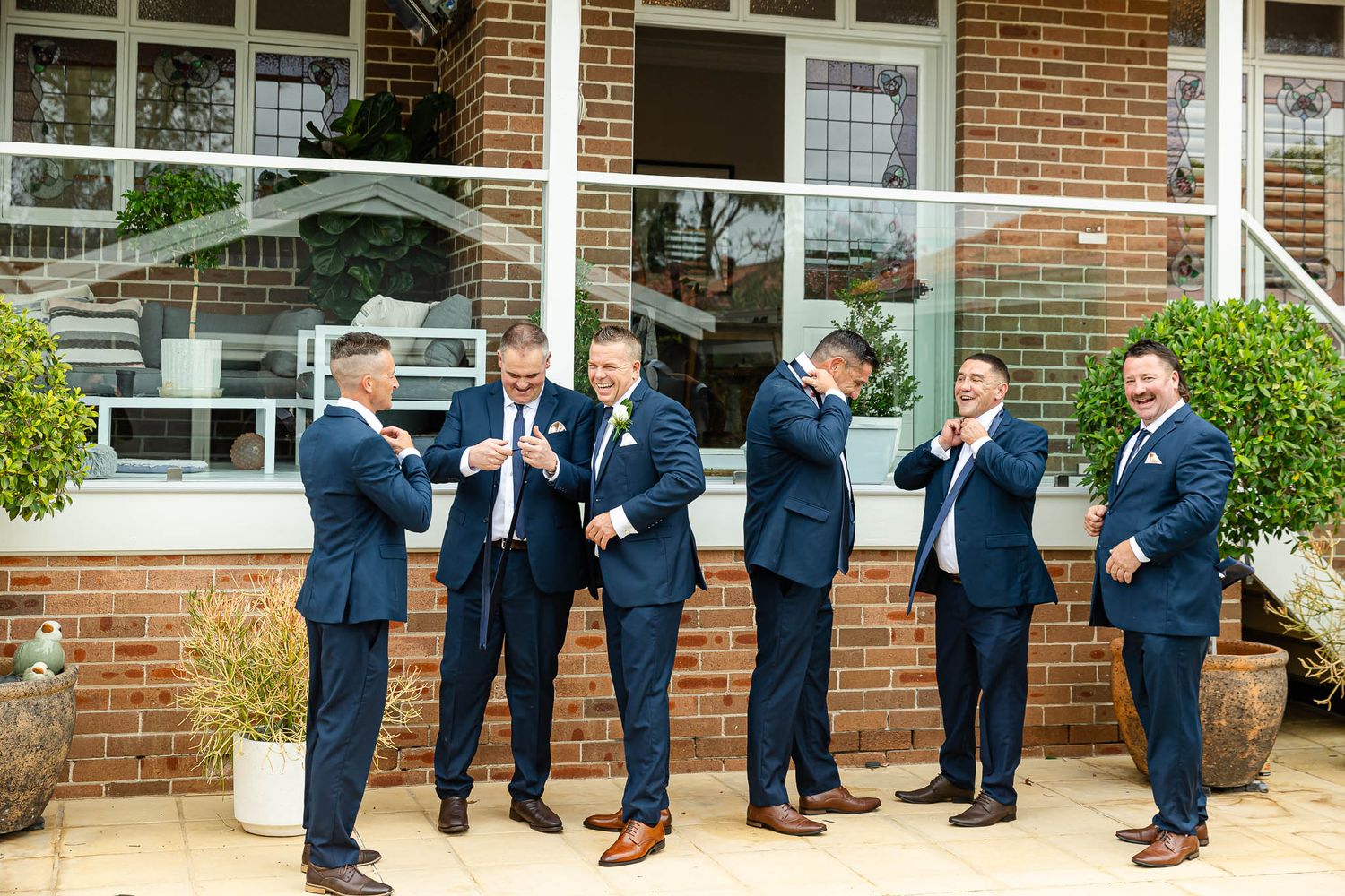 Panoramic sequence of groomsmen in navy suits chatting and laughing together outside a brick building.