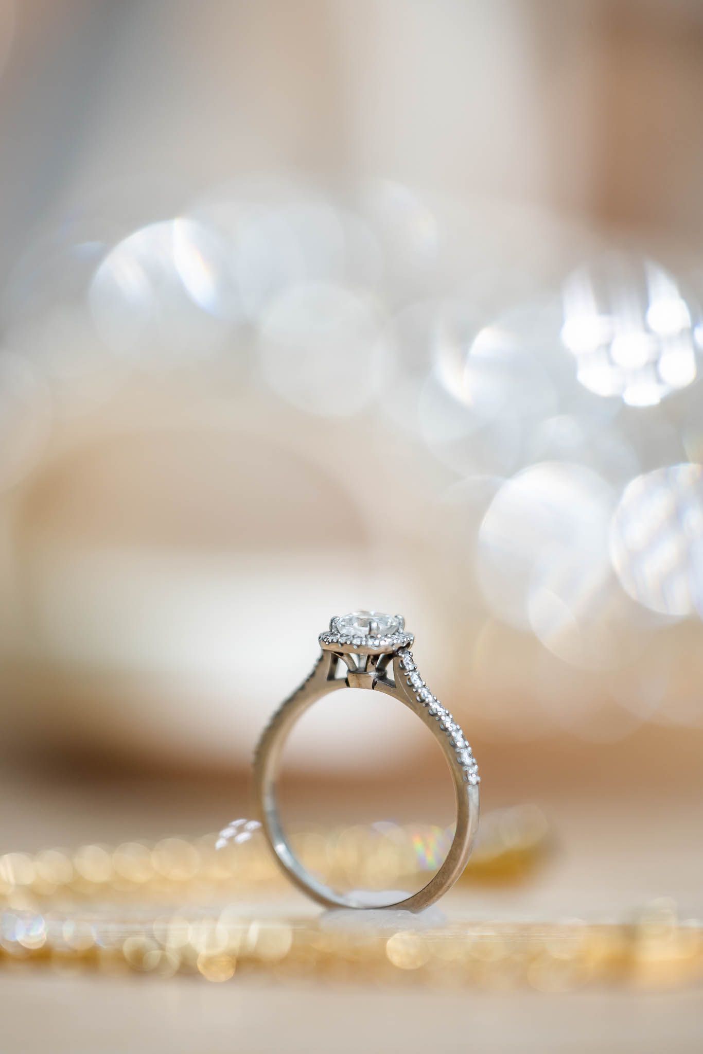 Elegant diamond engagement ring with halo setting photographed against soft bokeh background.