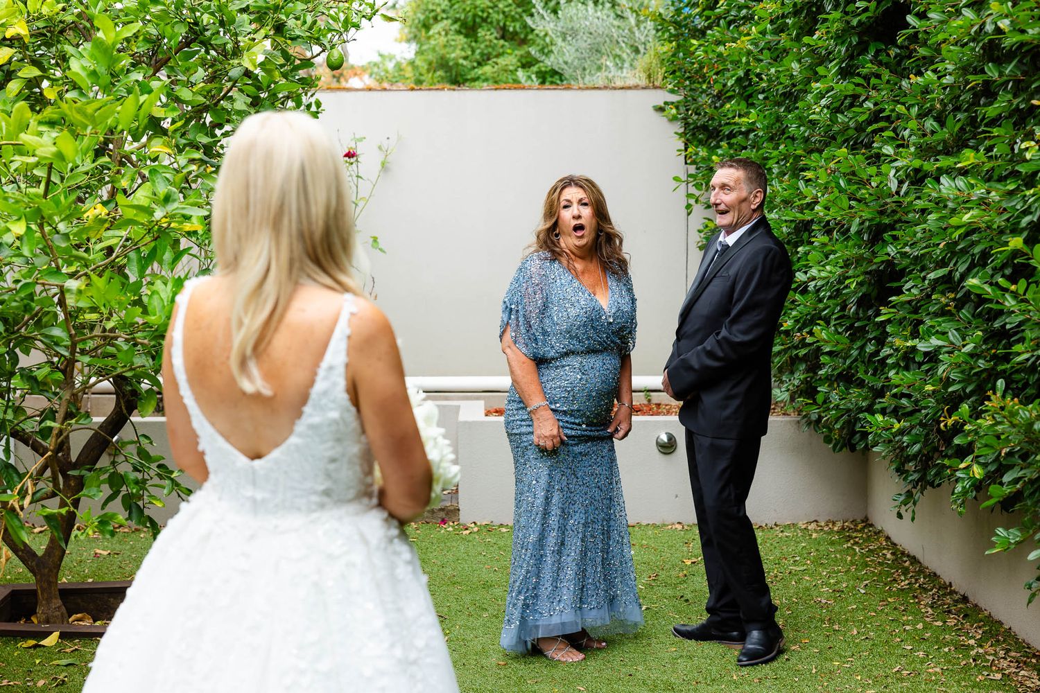 Outdoor garden wedding ceremony scene with guests gathered among lush green foliage on a sunny day.