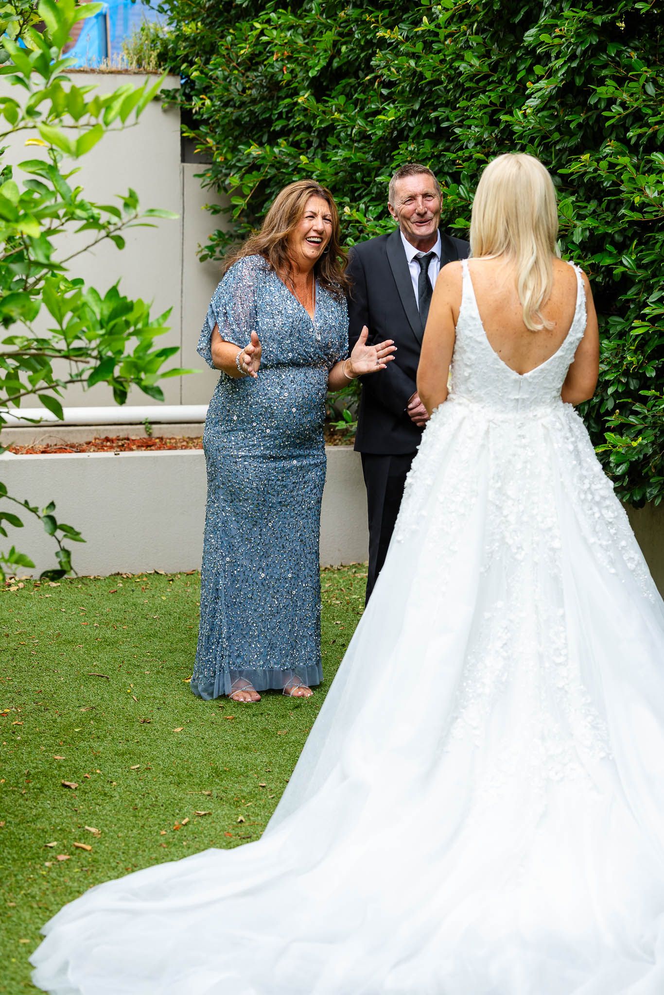 Wedding guests share a joyful moment with bride in elegant white gown with long train on garden lawn.