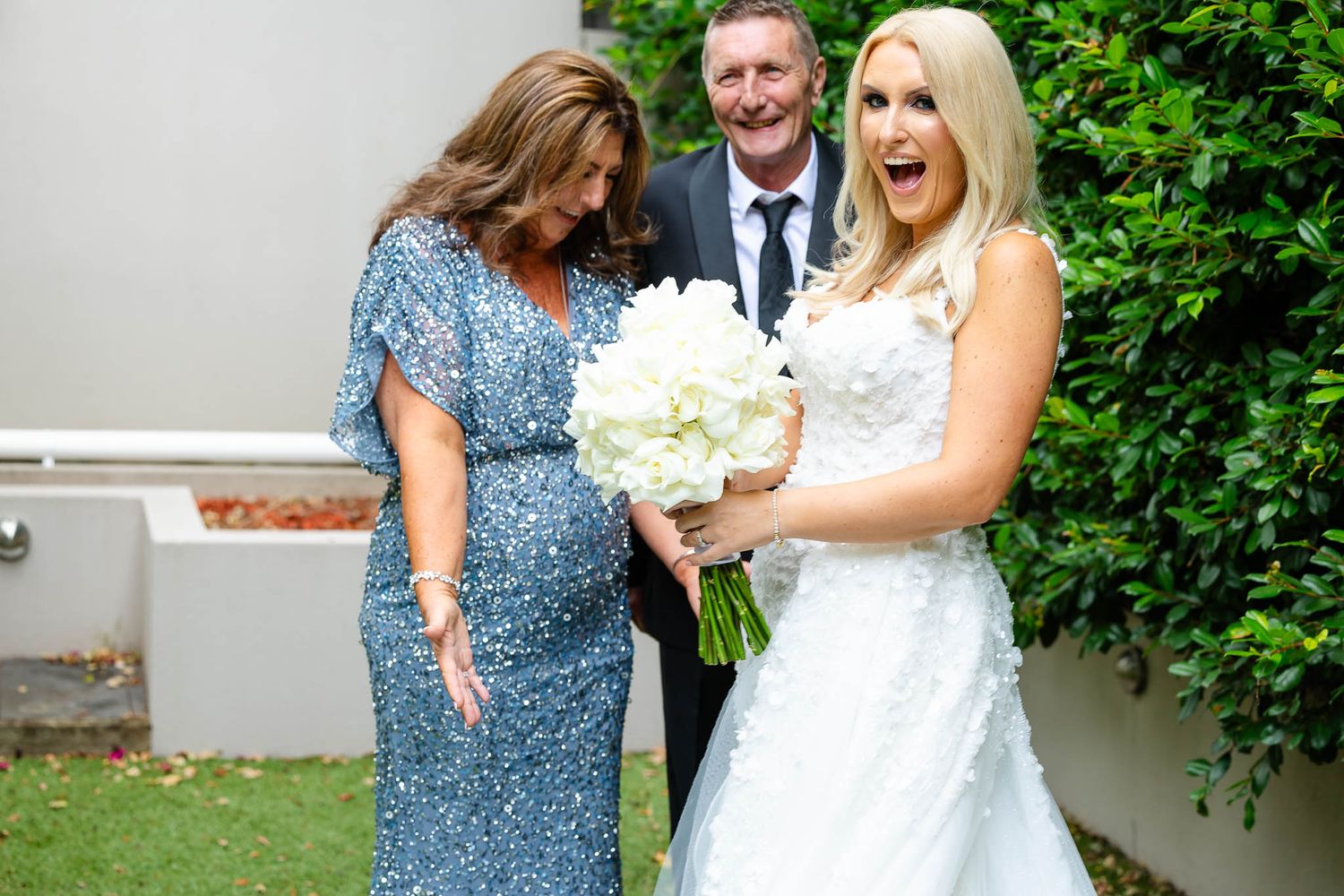 A joyful bride in a white gown shares a candid laughing moment with a guest in a blue dress at an outdoor wedding.