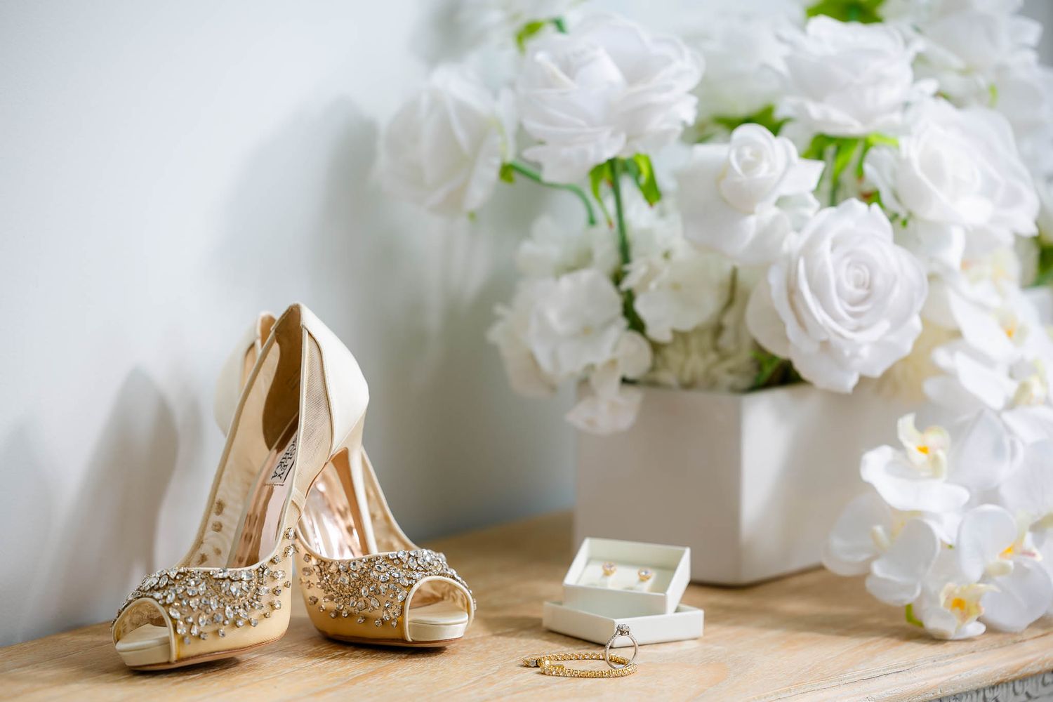 Elegant bridal accessories including sparkly heels and white floral arrangements displayed on white surface.
