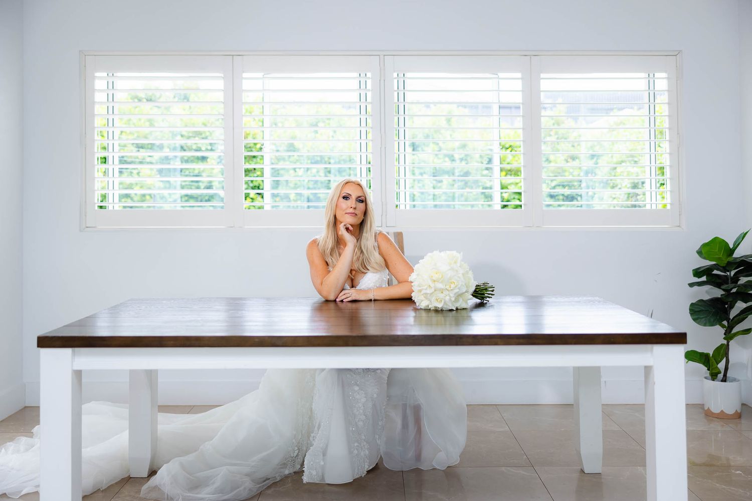 A bright white modern room with plantation shutters and a long wooden table.