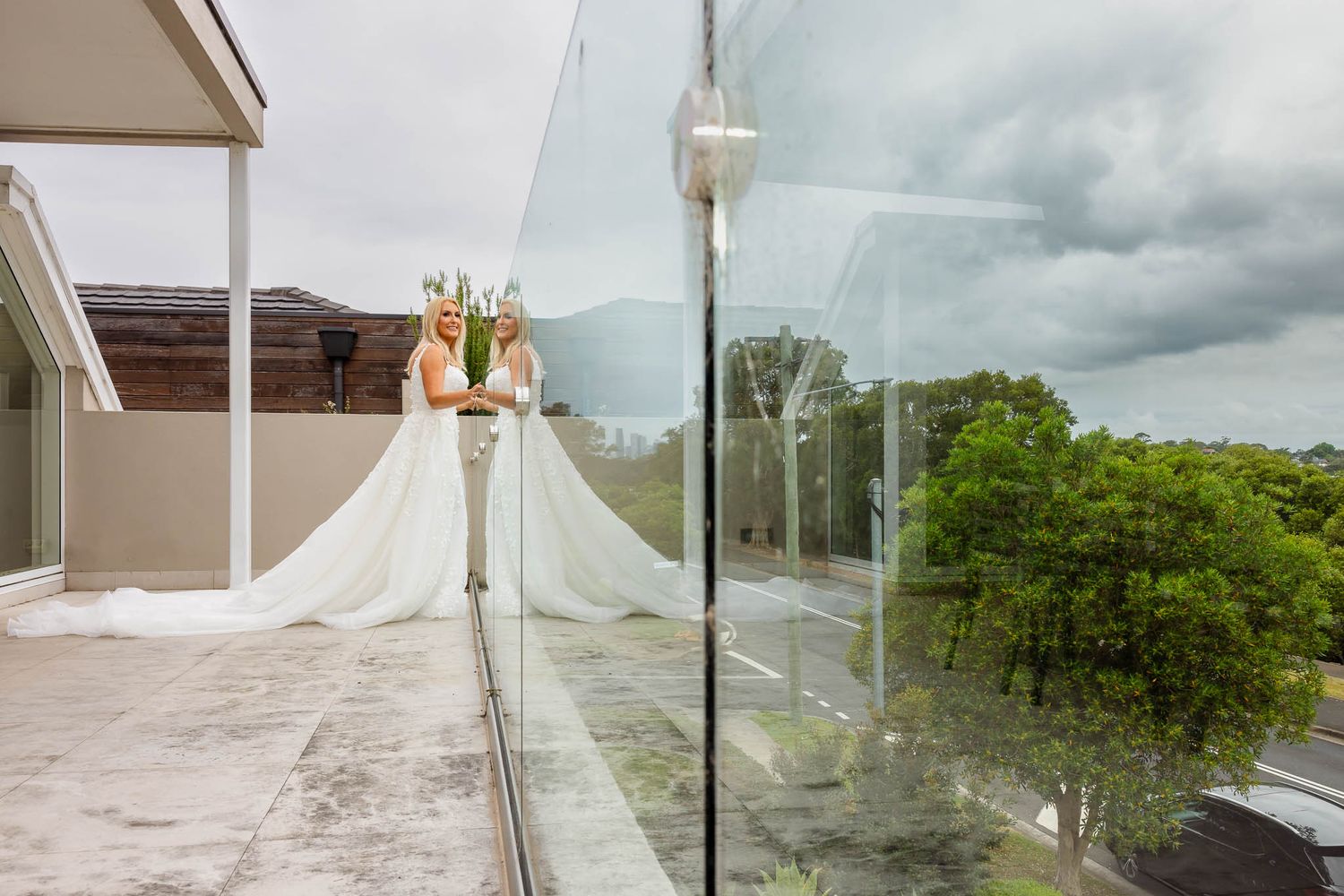 A bride in a flowing white gown poses elegantly against a scenic outdoor backdrop with cloudy skies.