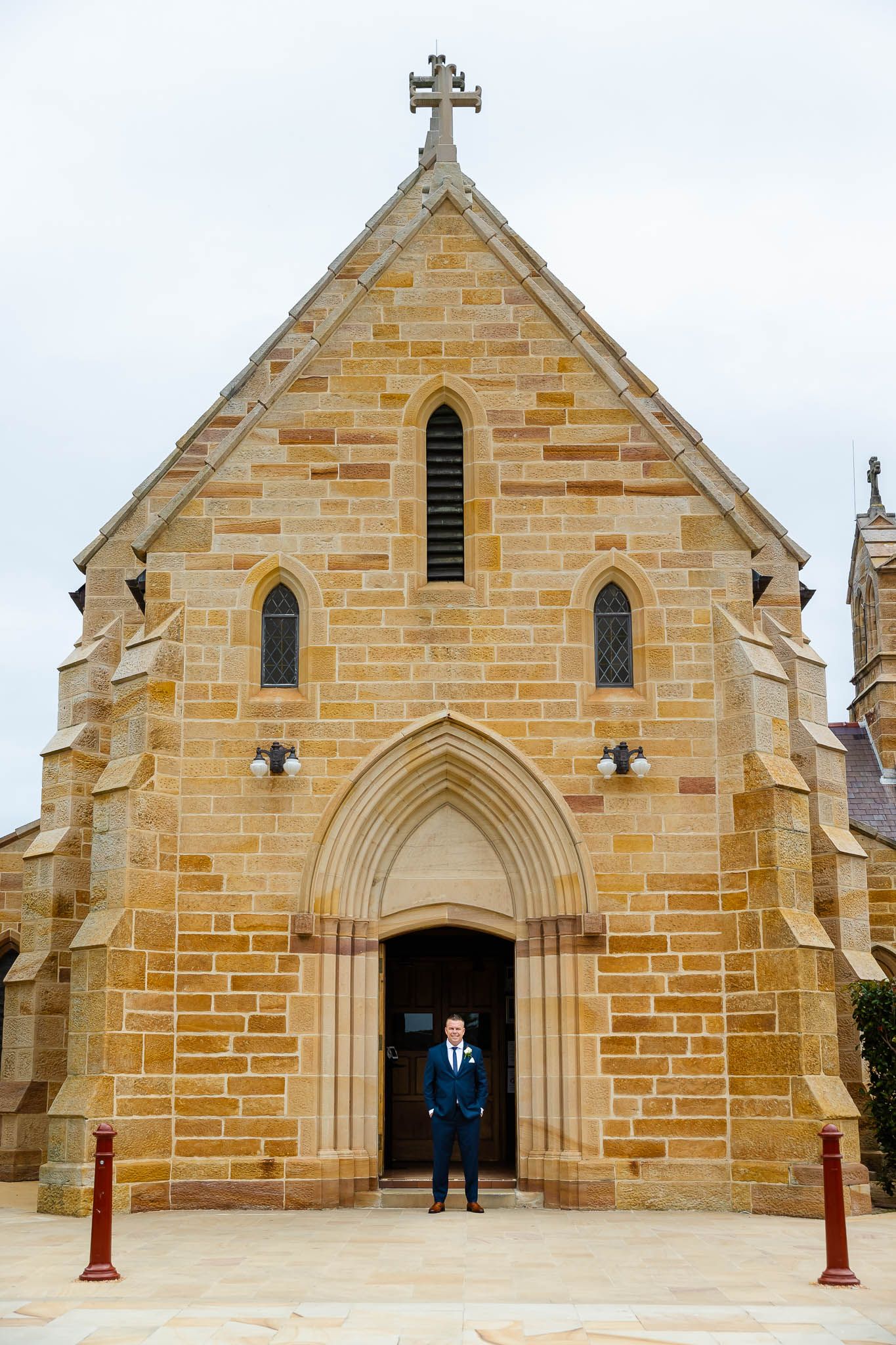 Historic sandstone church with Gothic architecture features a pointed archway entrance and cross on top of its gabled roof.