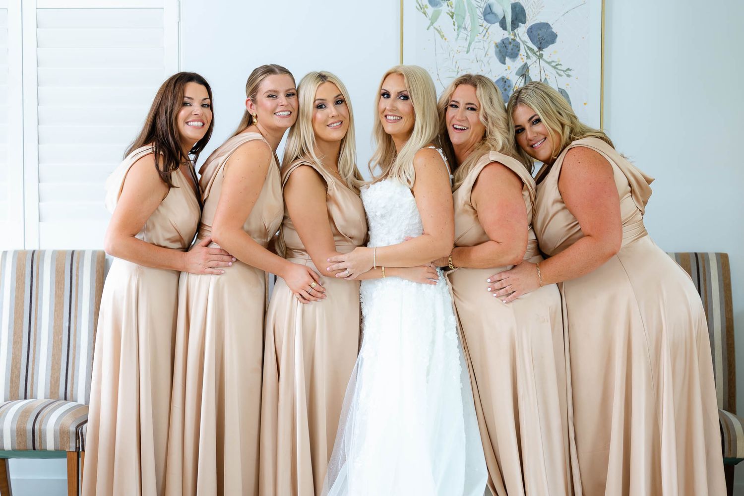A bridal party poses together wearing blush colored dresses and a white wedding gown.