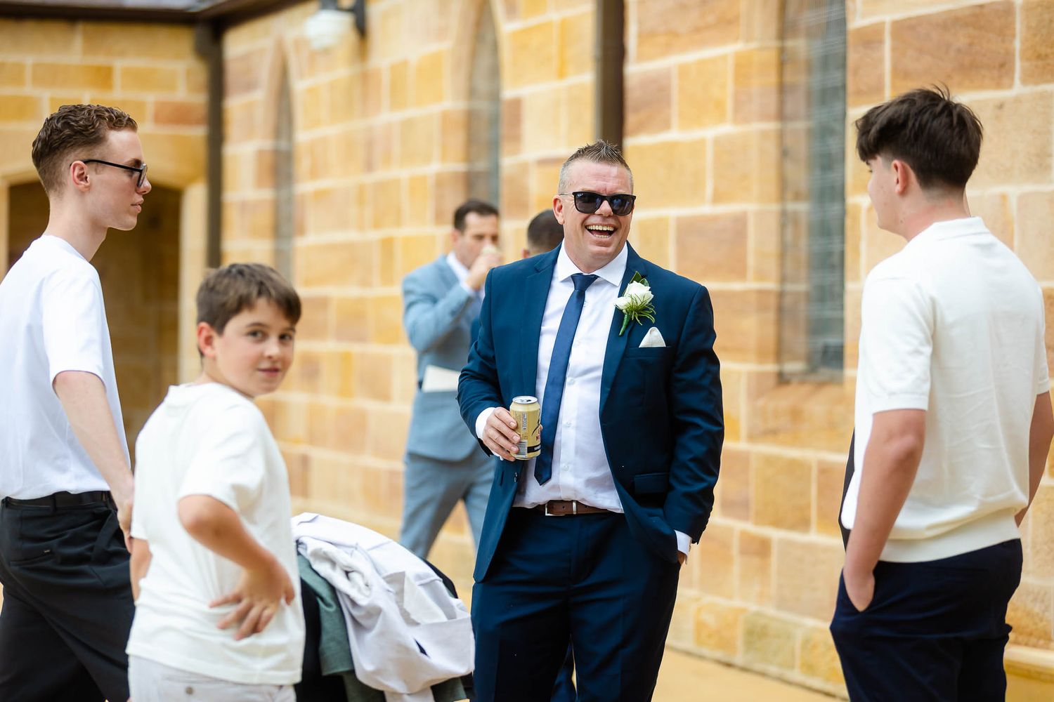 A group of people chatting outside a brick building, with one person wearing a navy suit and sunglasses.