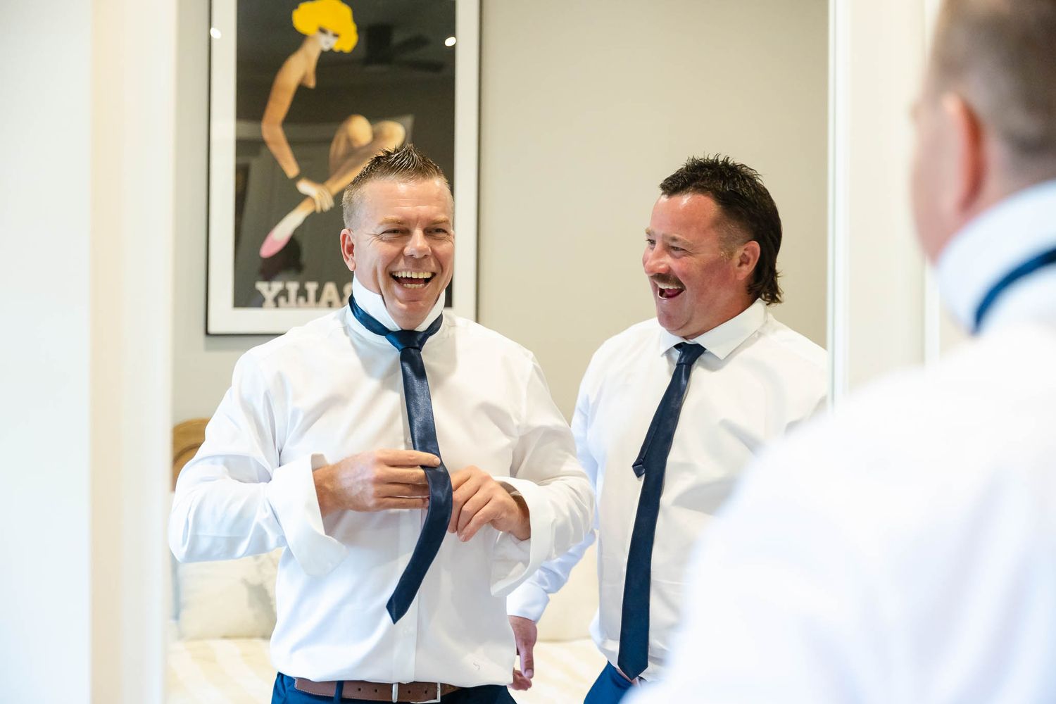 Groomsmen in white shirts and blue ties sharing laughter while getting ready for wedding celebration.