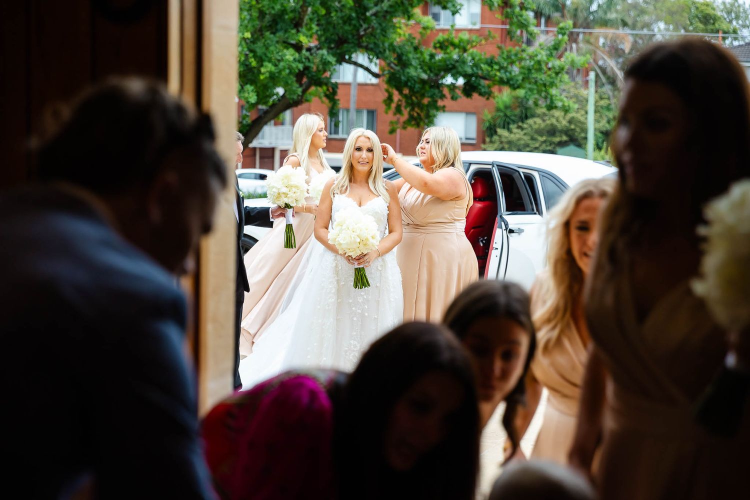 A bridal party in blush pink dresses arrives at a church entrance for a wedding ceremony.