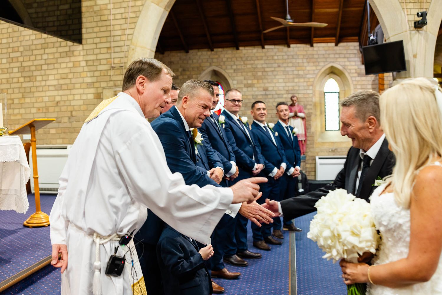 Wedding guests seated in church pews during ceremony while bride and groom exchange vows at the altar.