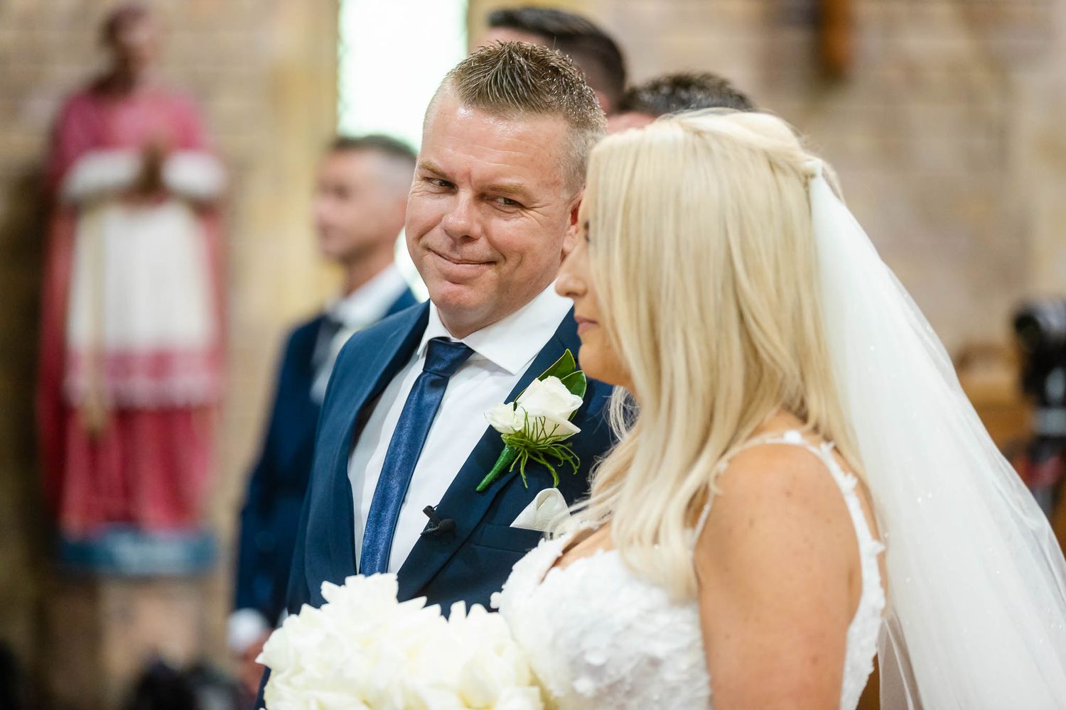 A bride and groom share a tender moment during their wedding ceremony in a beautiful stone church setting.