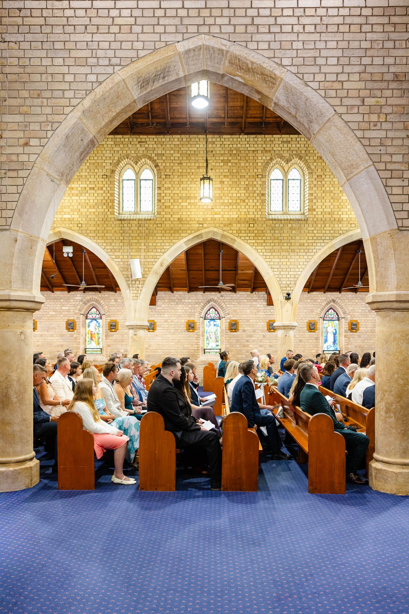 Church congregation sits in wooden pews under brick arches during a religious service in a traditional sanctuary.
