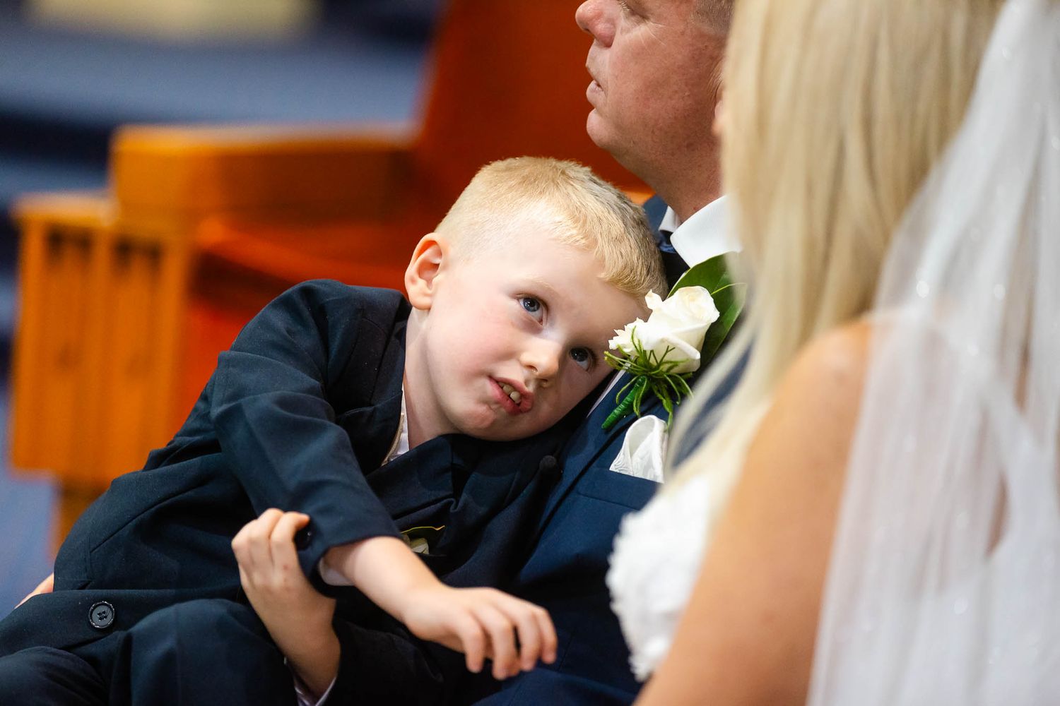 A young boy in formal attire appears tired and sleepy during what seems to be a wedding ceremony.