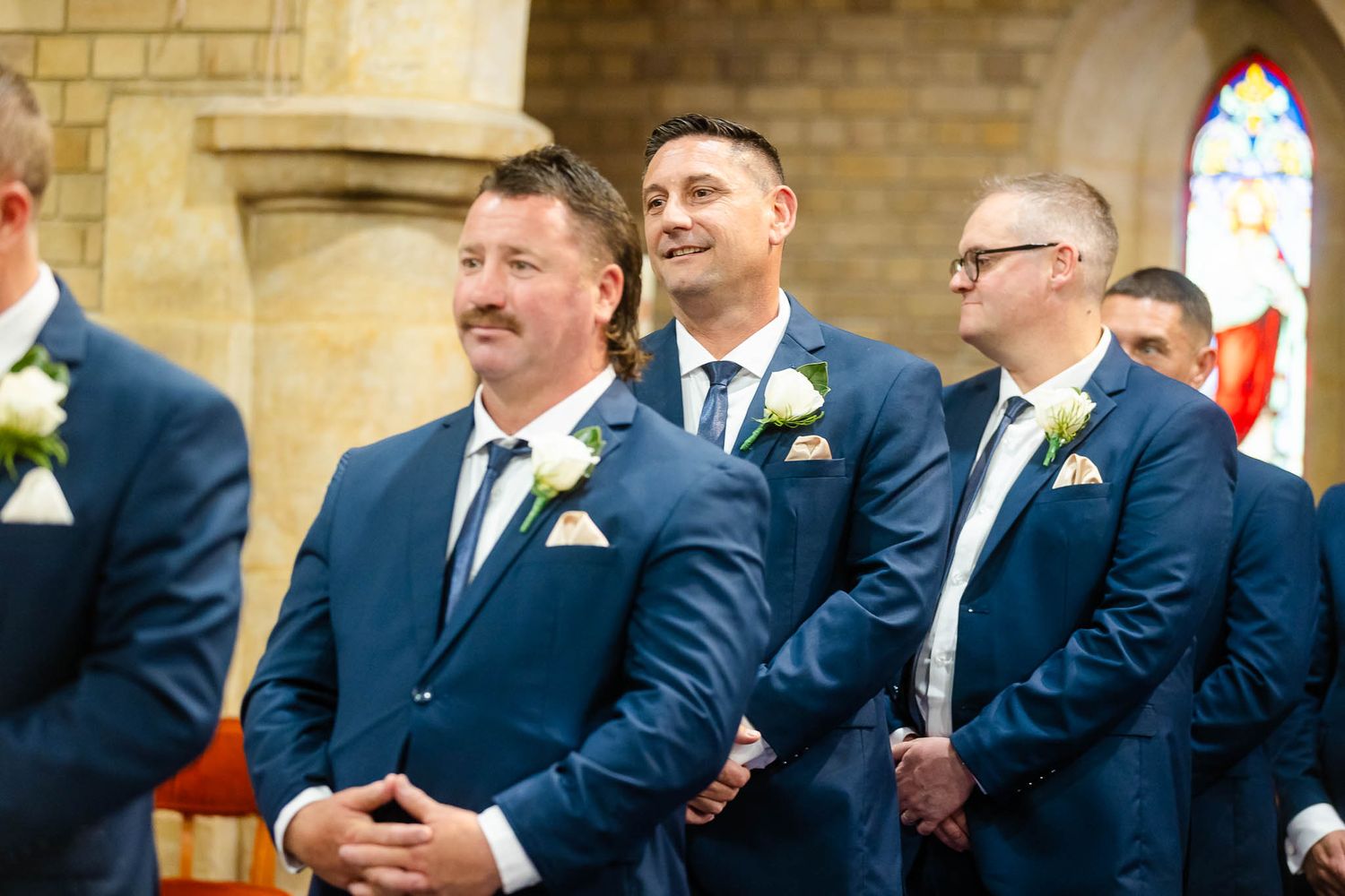 Groomsmen in navy blue suits standing together at the altar during a wedding ceremony.