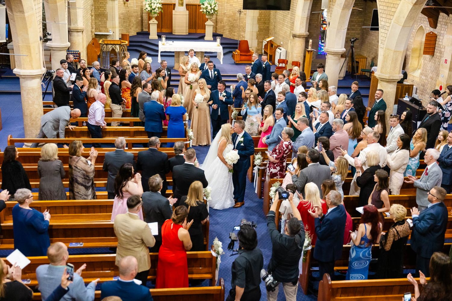 A large congregation stands together during a church service in a traditional sanctuary with wooden pews.