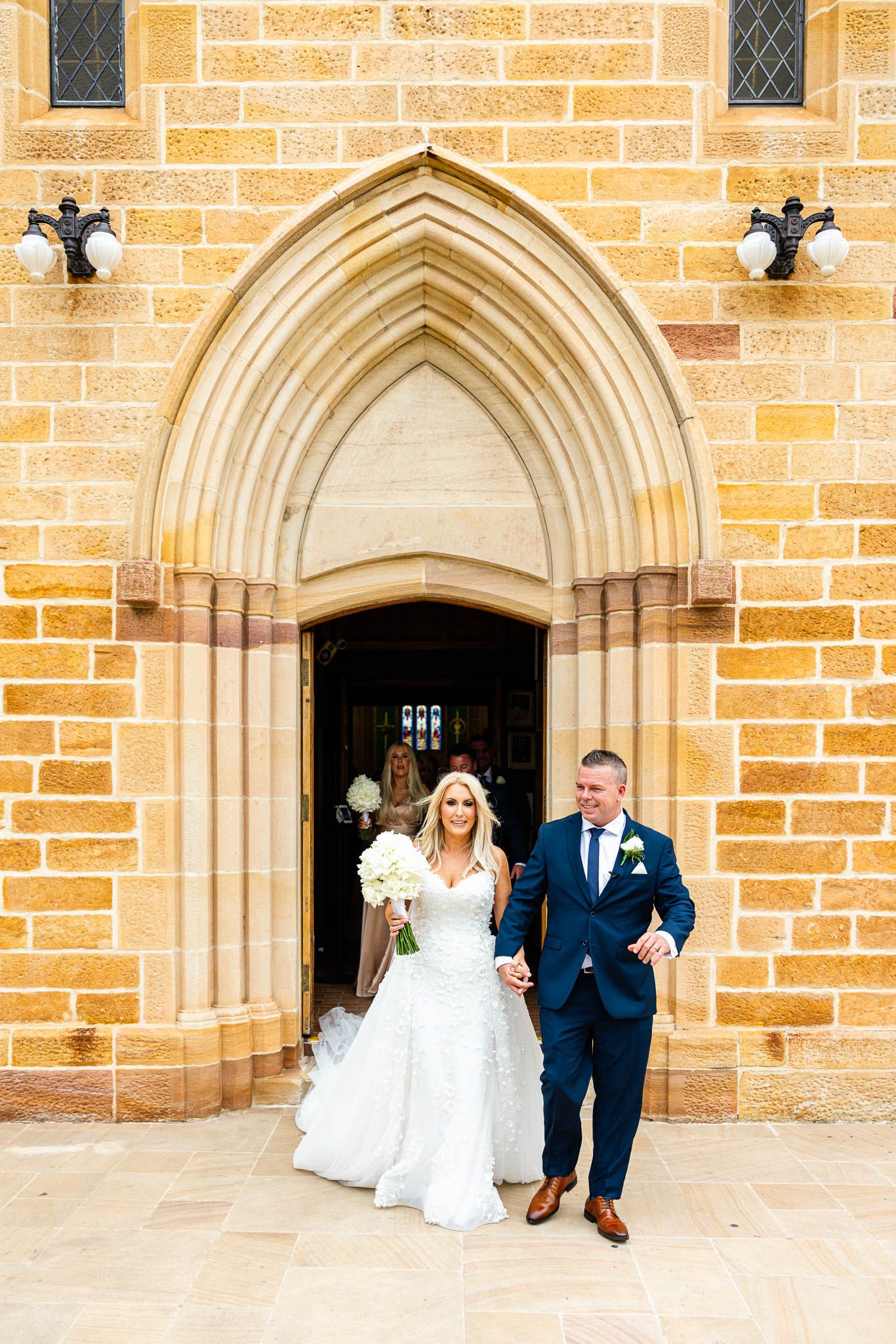 A series of gothic stone archways with couples standing beneath them at a historic church building.