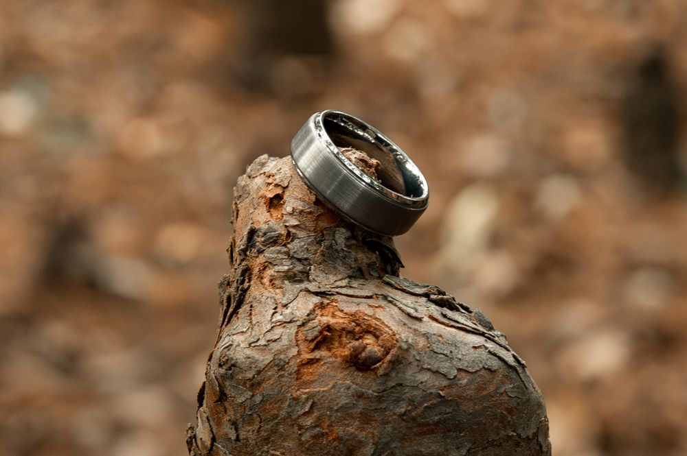 A silver wedding ring balances on a rough brown rock surface in natural lighting.