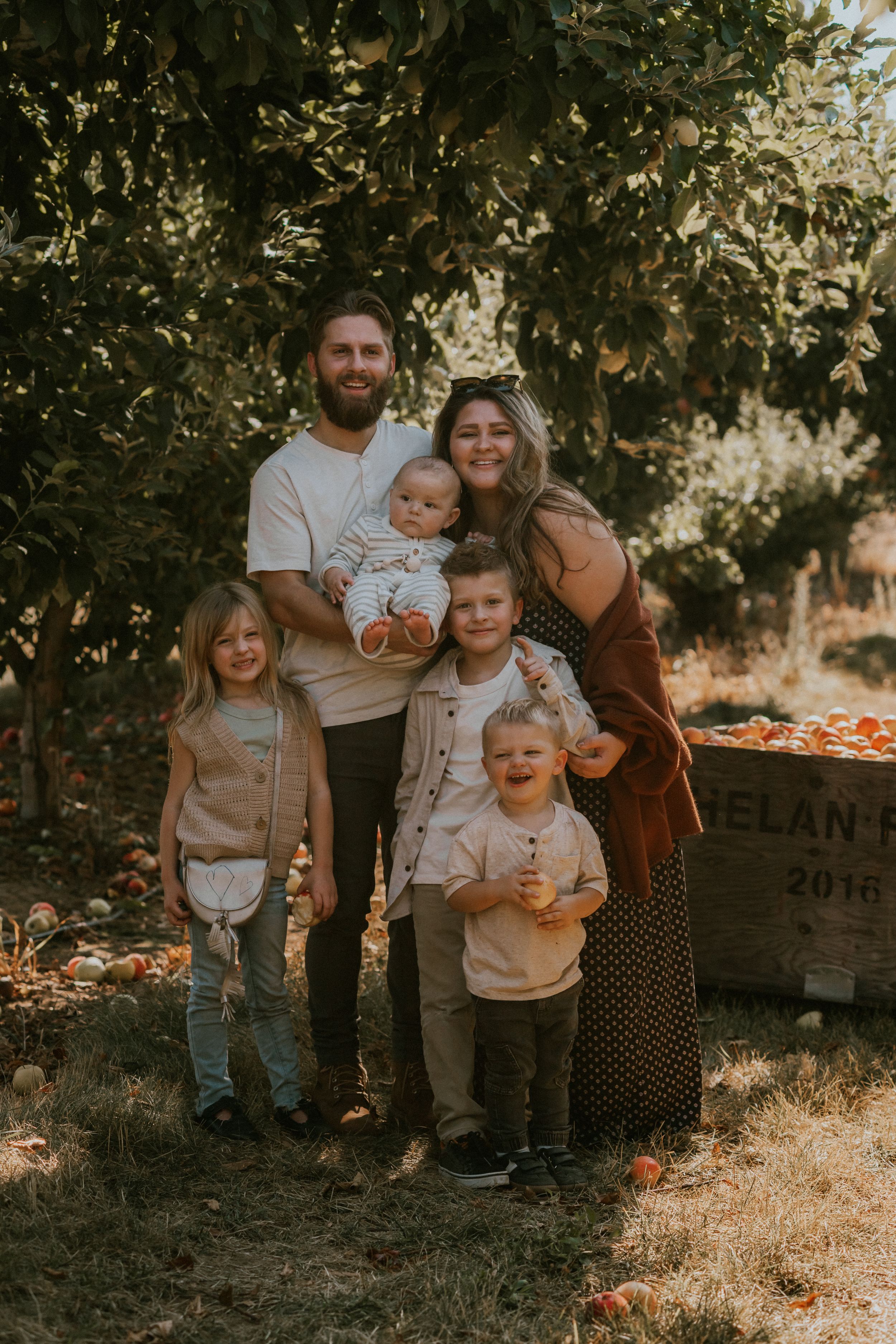 Family portrait session in a golden autumn setting with sunlit trees and fallen leaves creating a warm outdoor atmosphere.