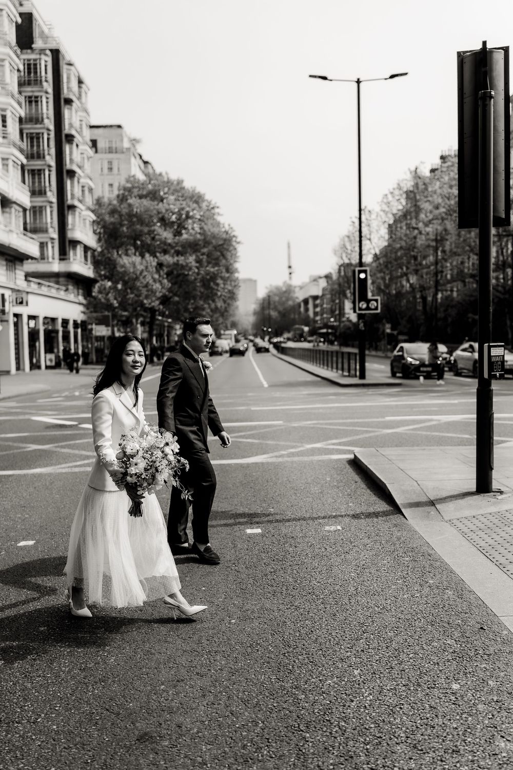 A couple in wedding attire walks down a city street in black and white photography.