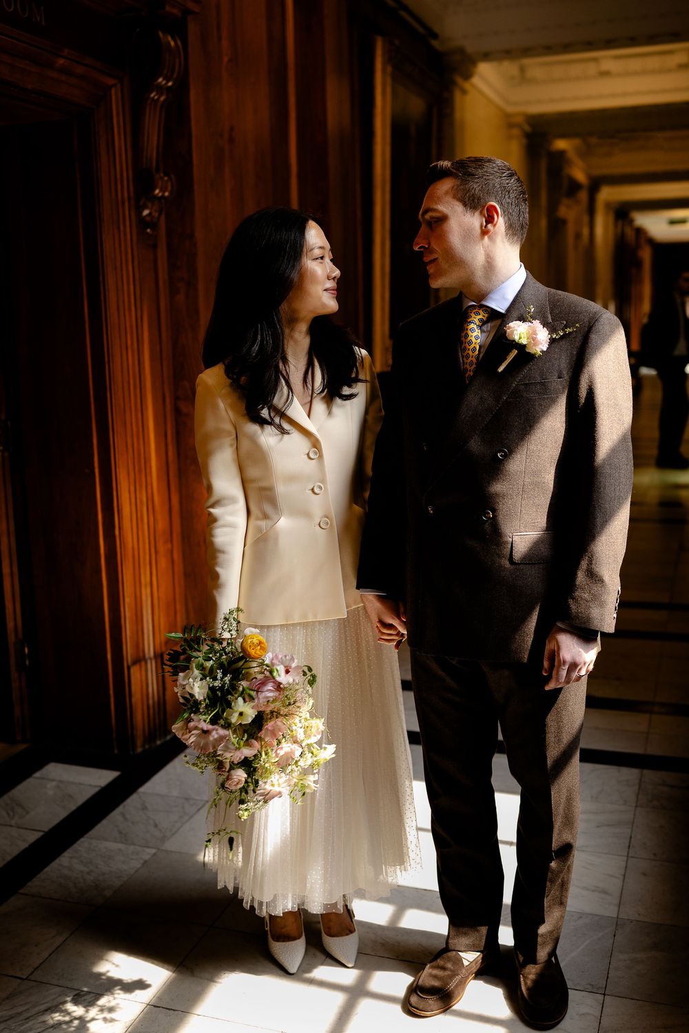 A romantic wedding couple stands in warm sunlight streaming through wooden hallway windows in vintage style photos.