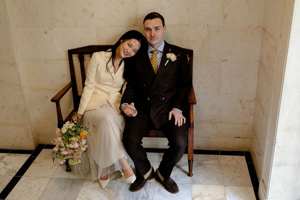 Wedding couple posing together against a light colored wall in an indoor setting.