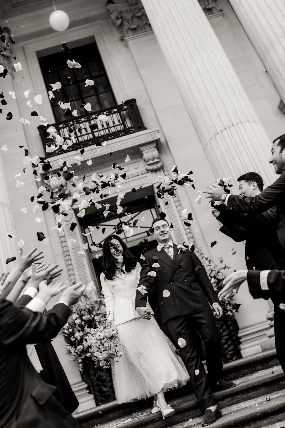 Wedding celebration moment with guests tossing confetti outside a columned building entrance.