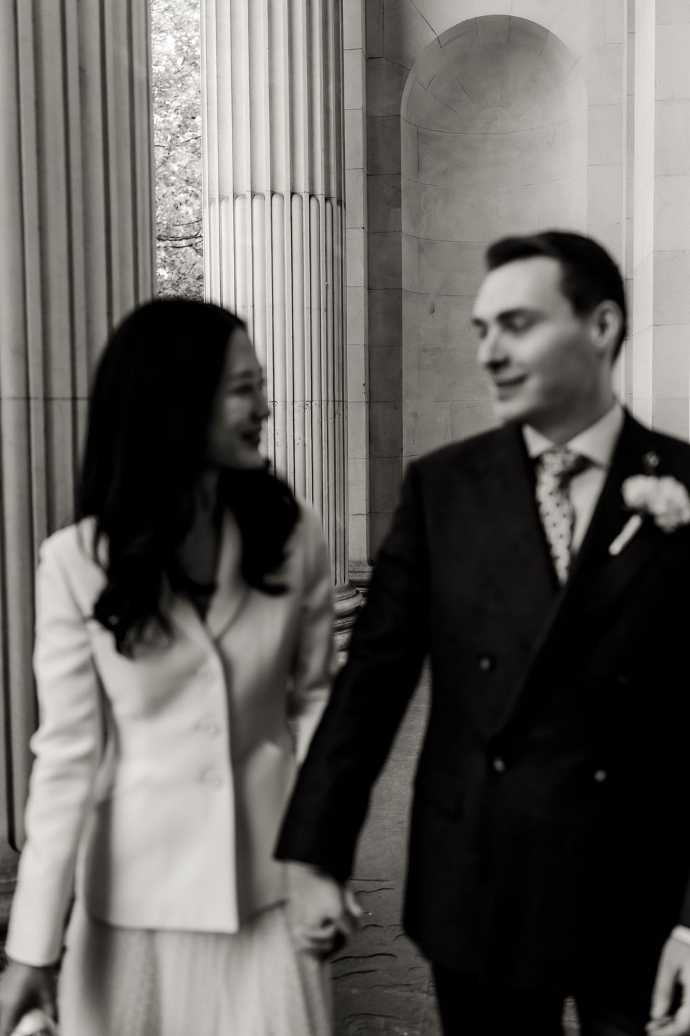 Wedding couple walks together through a classic columned hallway with white architectural details.