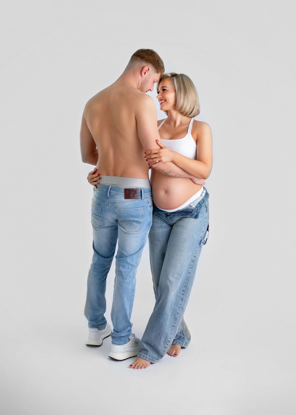 A couple wearing jeans embraces intimately in a white studio setting, shown in multiple similar poses.