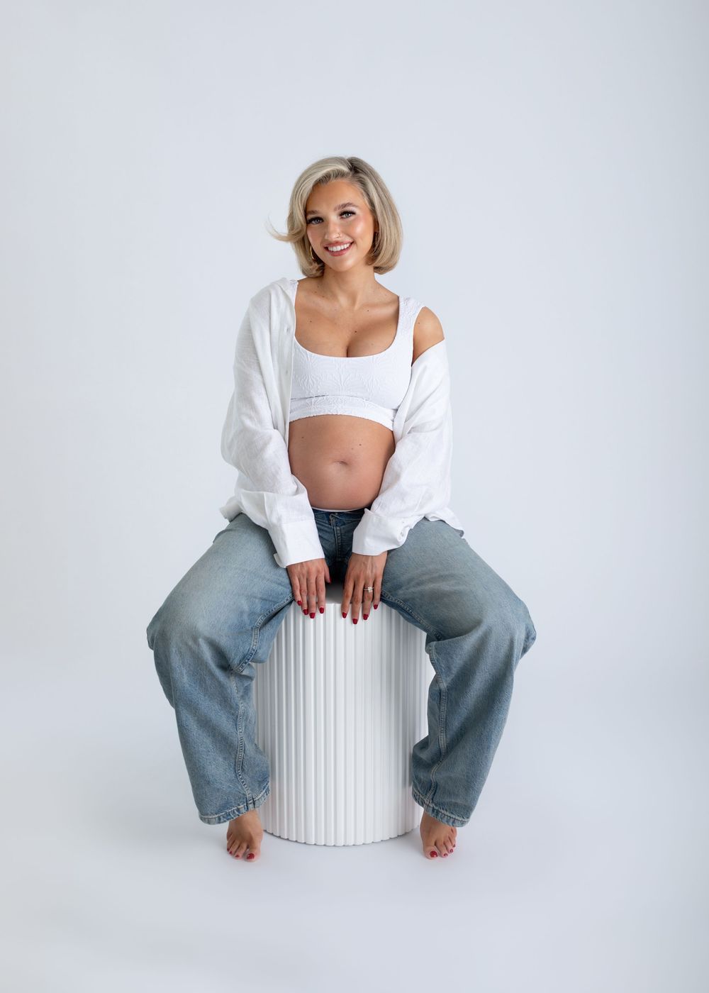 A sequence of photos showing someone in a white top and wide-leg jeans sitting on a white cylindrical stool against a white background.