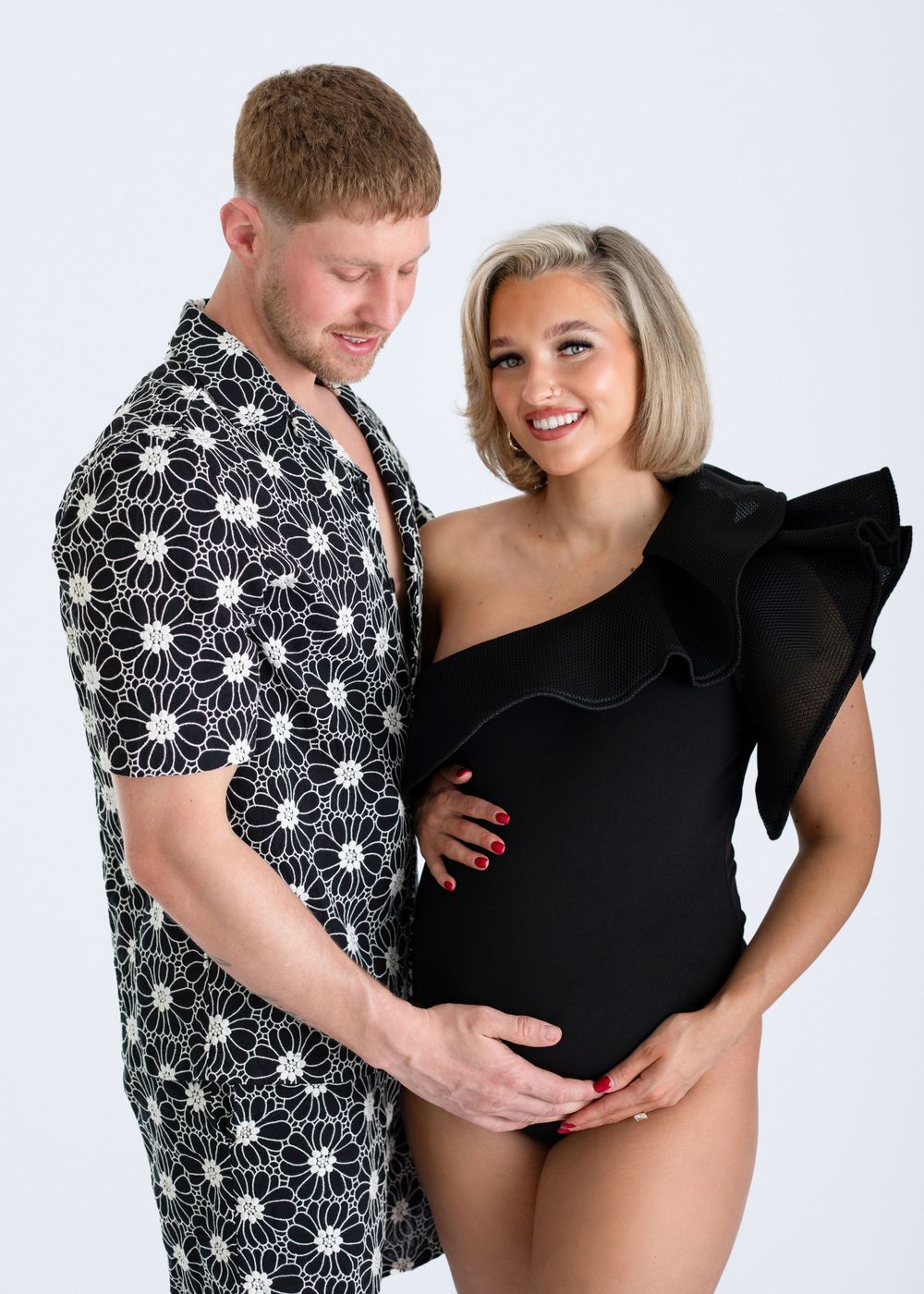 A couple in coordinating black and white outfits pose together against a light background for a maternity photo.