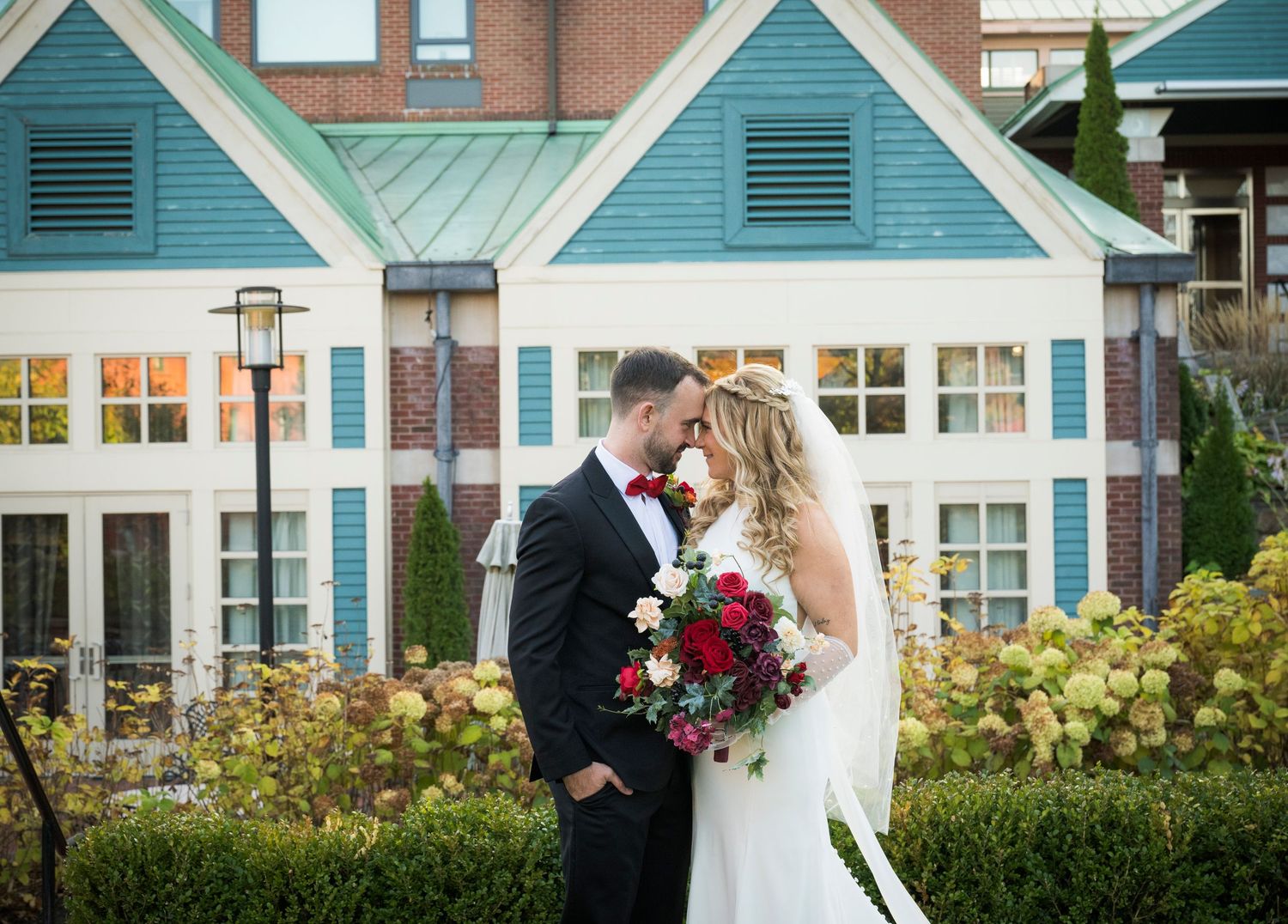 A couple shares a romantic moment in front of blue and white coastal buildings during a wedding celebration.