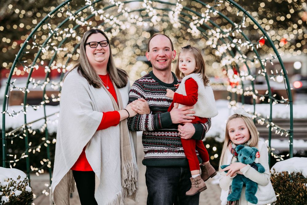 Family enjoys outdoor winter photo session with twinkling lights and festive holiday decorations in the background.