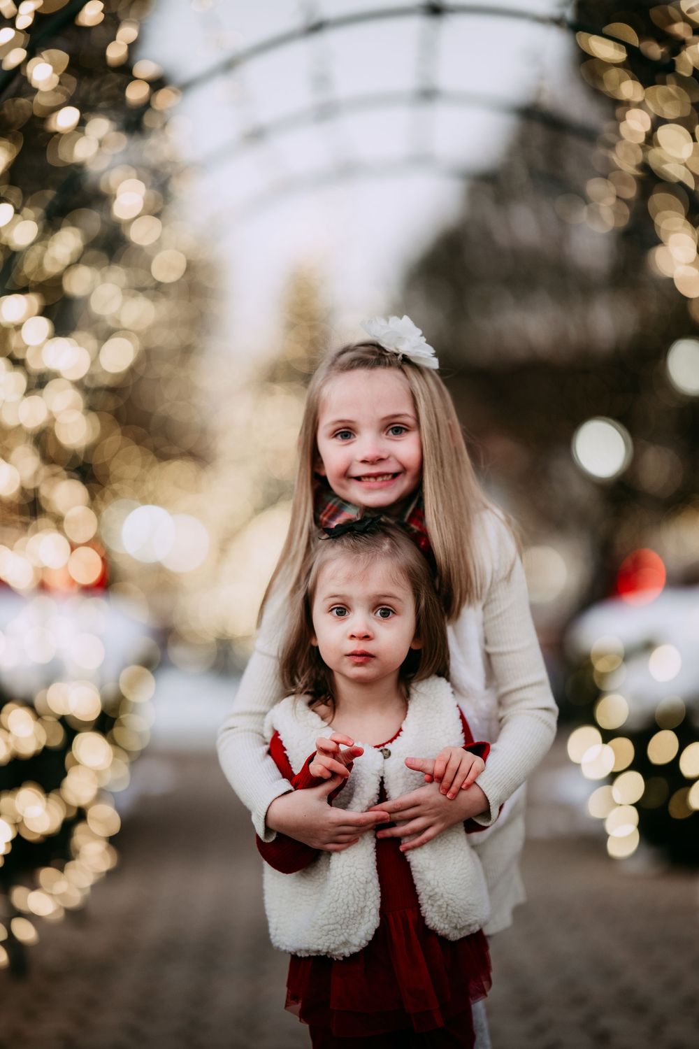 Three photos of a child in a burgundy dress against a bokeh background of holiday lights and trees.