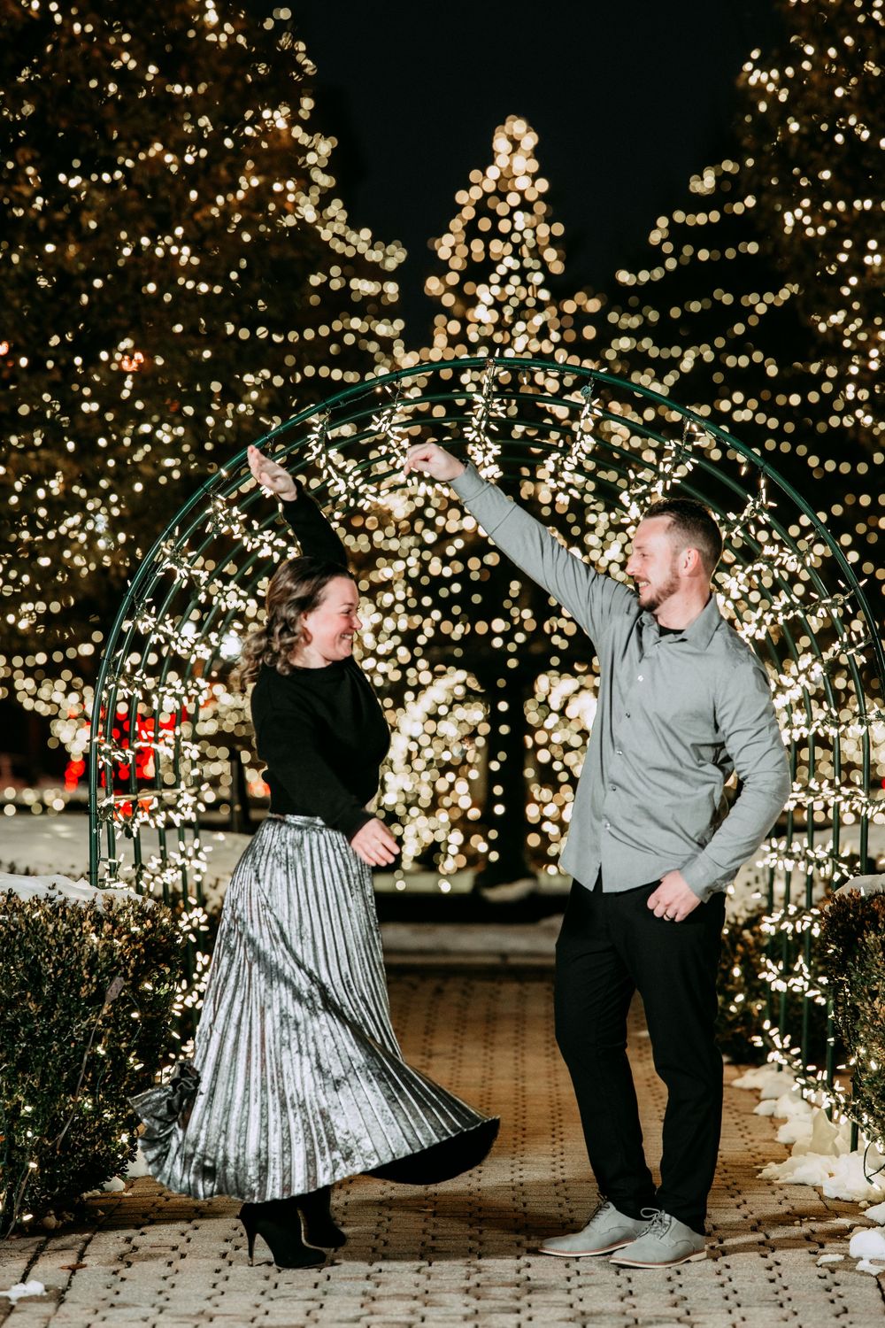 A couple dances together under a magical archway decorated with twinkling Christmas lights at night.