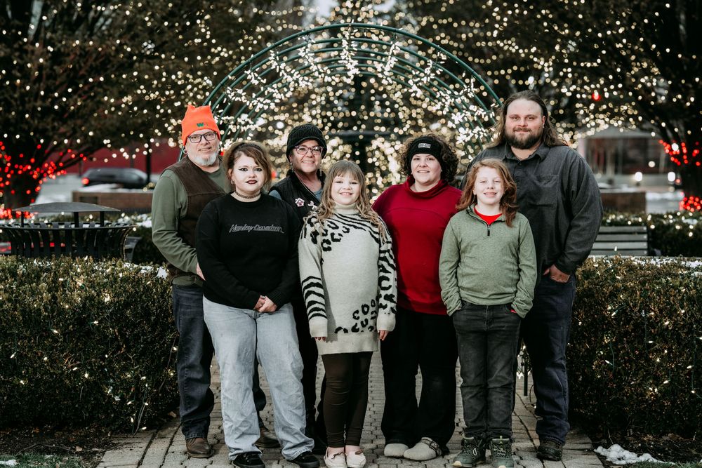A group poses together outdoors for a winter holiday photo with festive decorations and lights in the background.