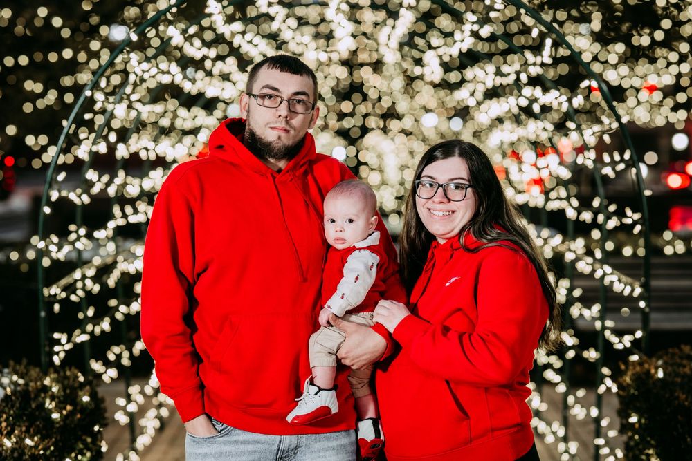 A family wearing matching red sweaters poses for holiday photos in front of twinkling Christmas lights.