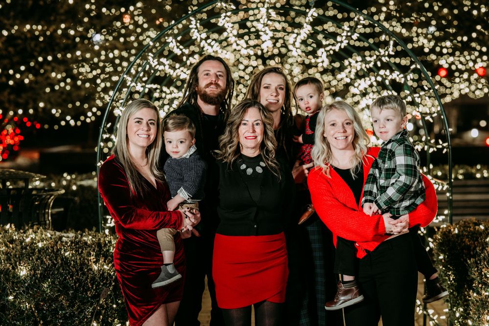 A group poses together outdoors at night with festive Christmas lights twinkling in the background.