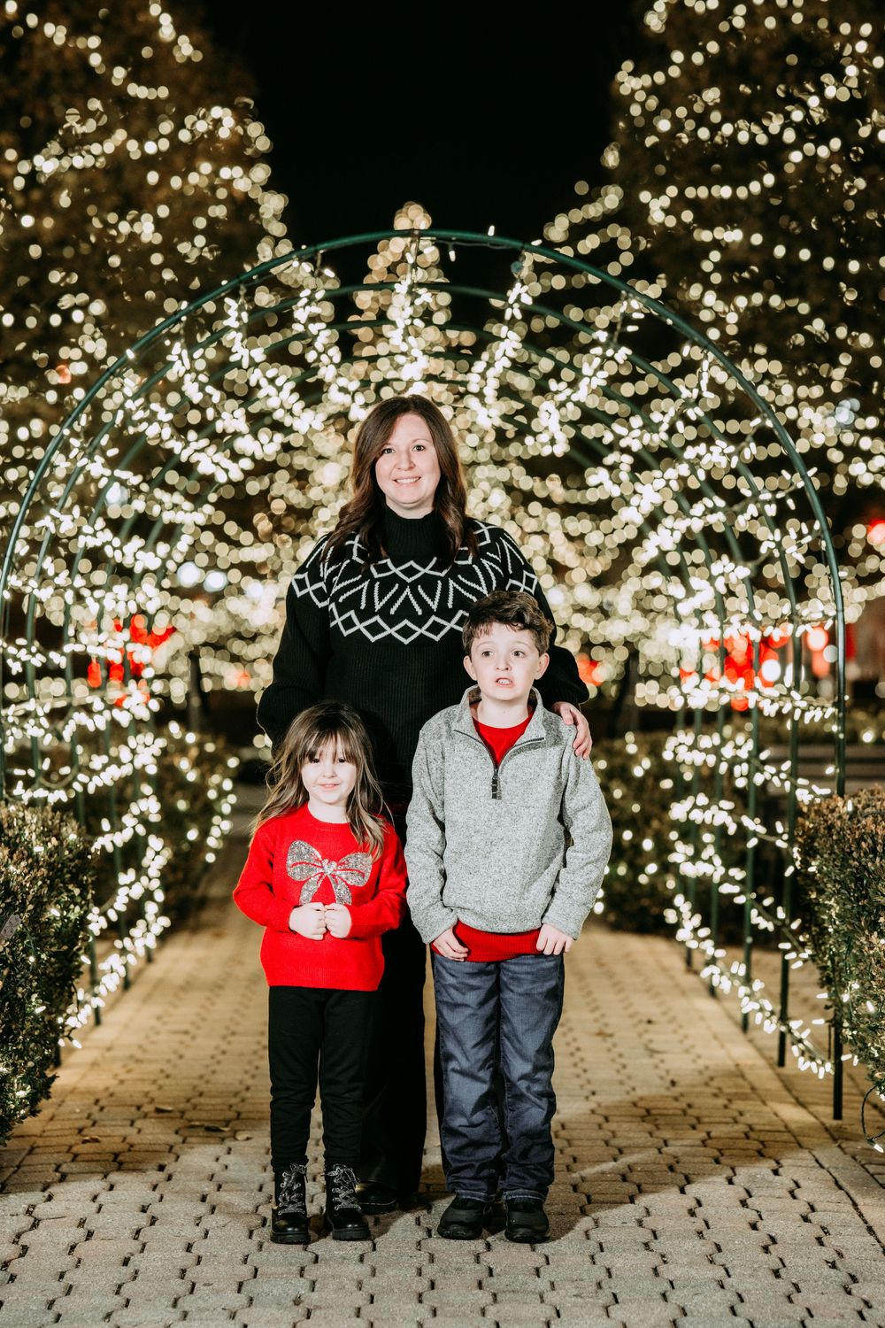 Family portrait series with holiday lights in background showing different poses on stone pathway.