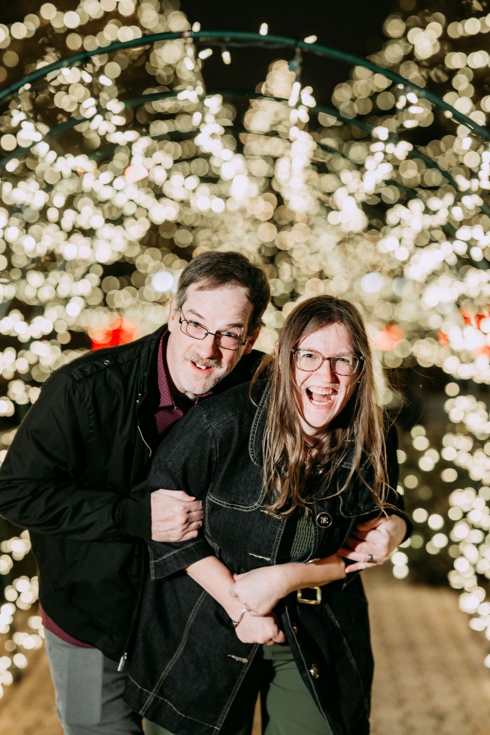 A couple shares a joyful moment together against a backdrop of sparkling bokeh lights at night.