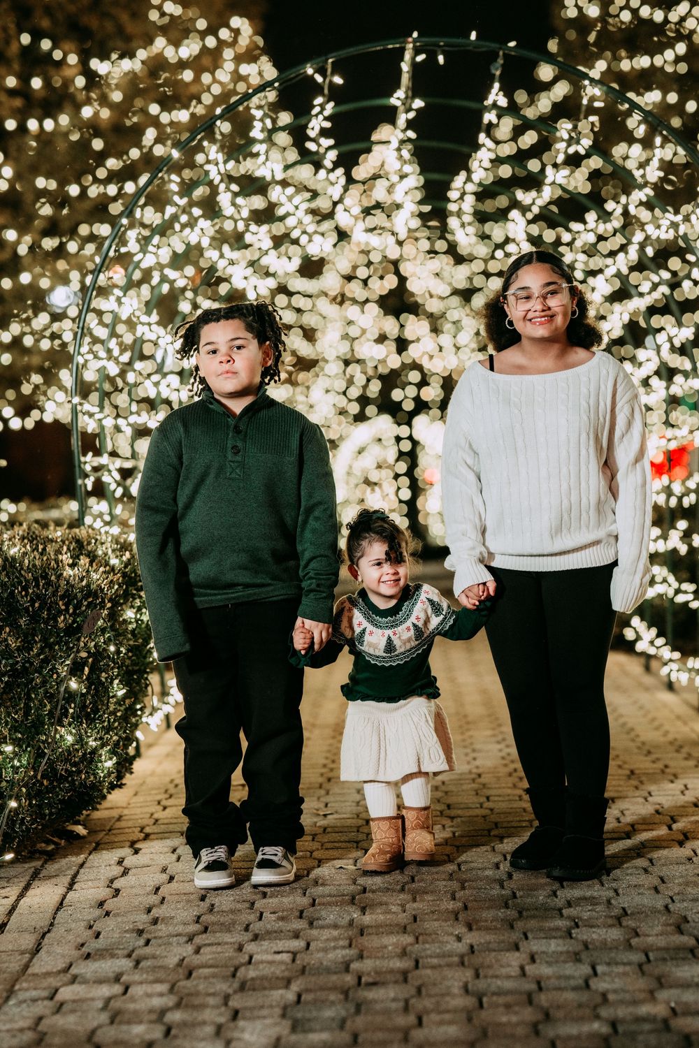 Family walking together on brick path with twinkling lights in background creating magical holiday atmosphere.