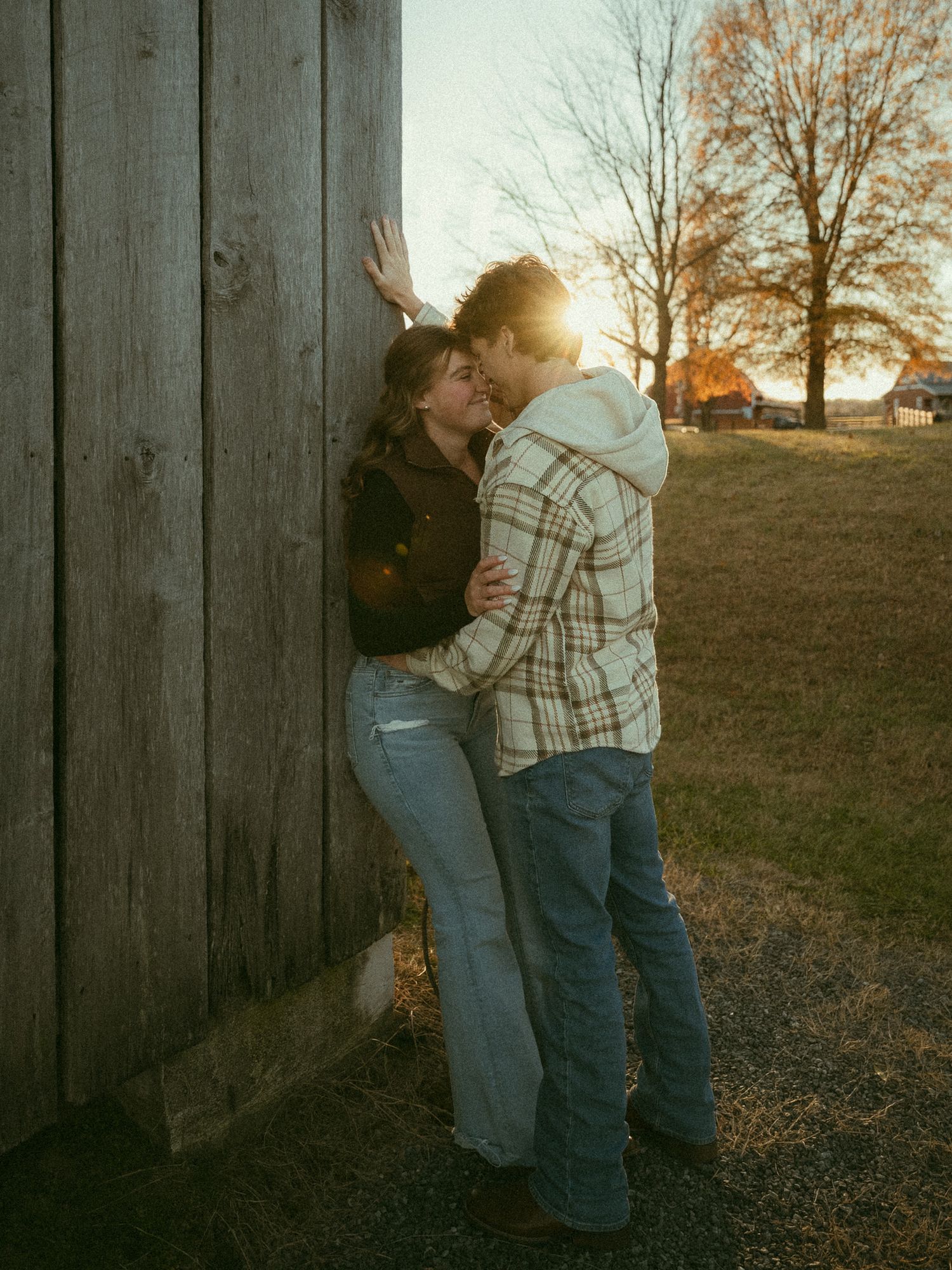 Romantic couple kissing against rustic wooden barn wall at golden sunset on a farm.