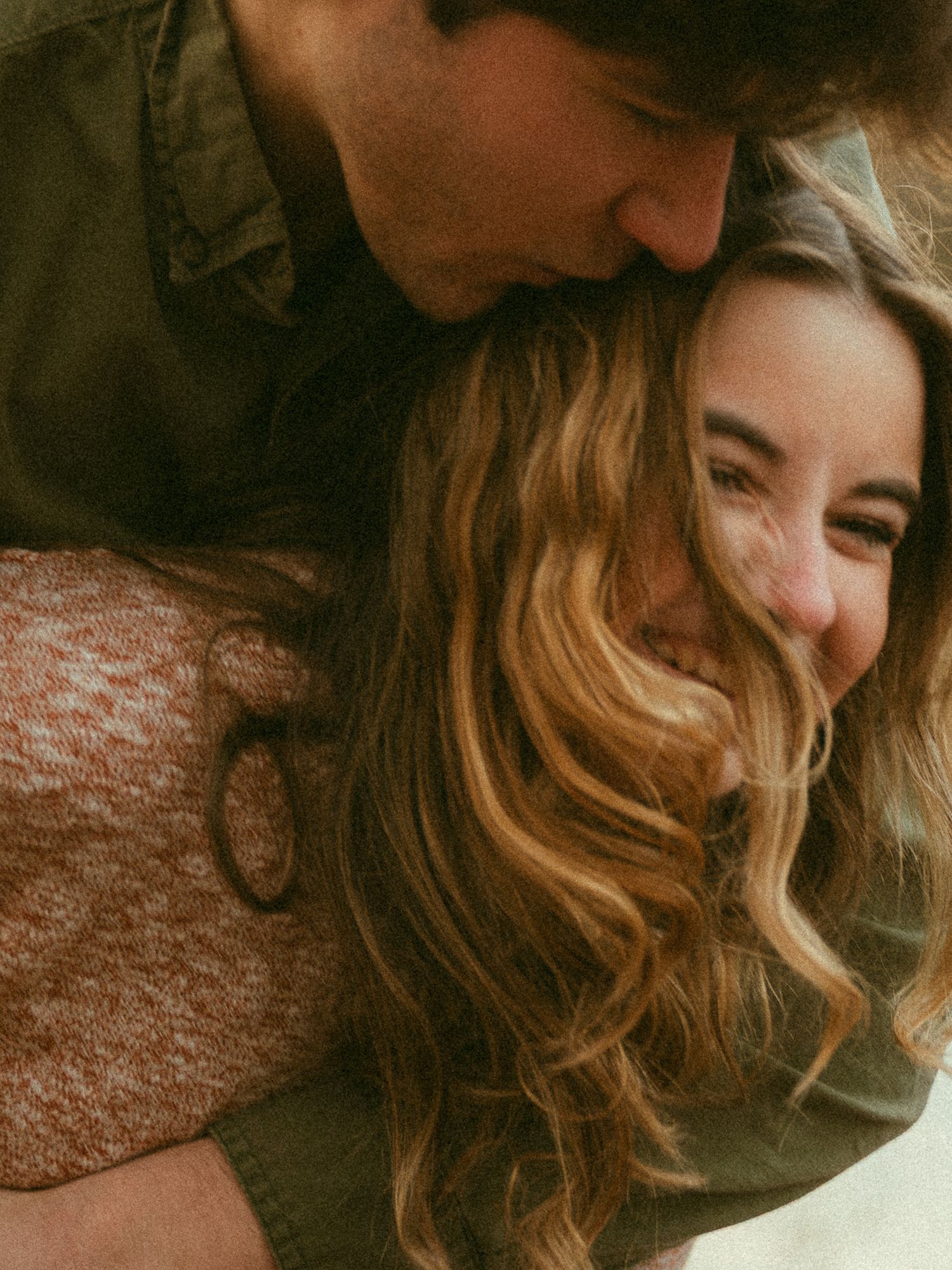 Young woman smiling joyfully as her partner kisses her head in a tender moment.