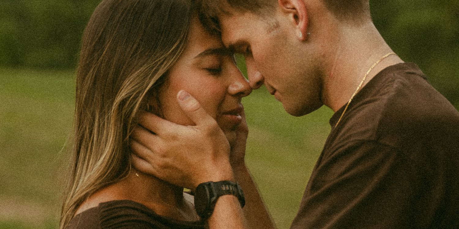 A couple shares a tender moment, the man gently cupping the womans face as they lean in close outdoors.