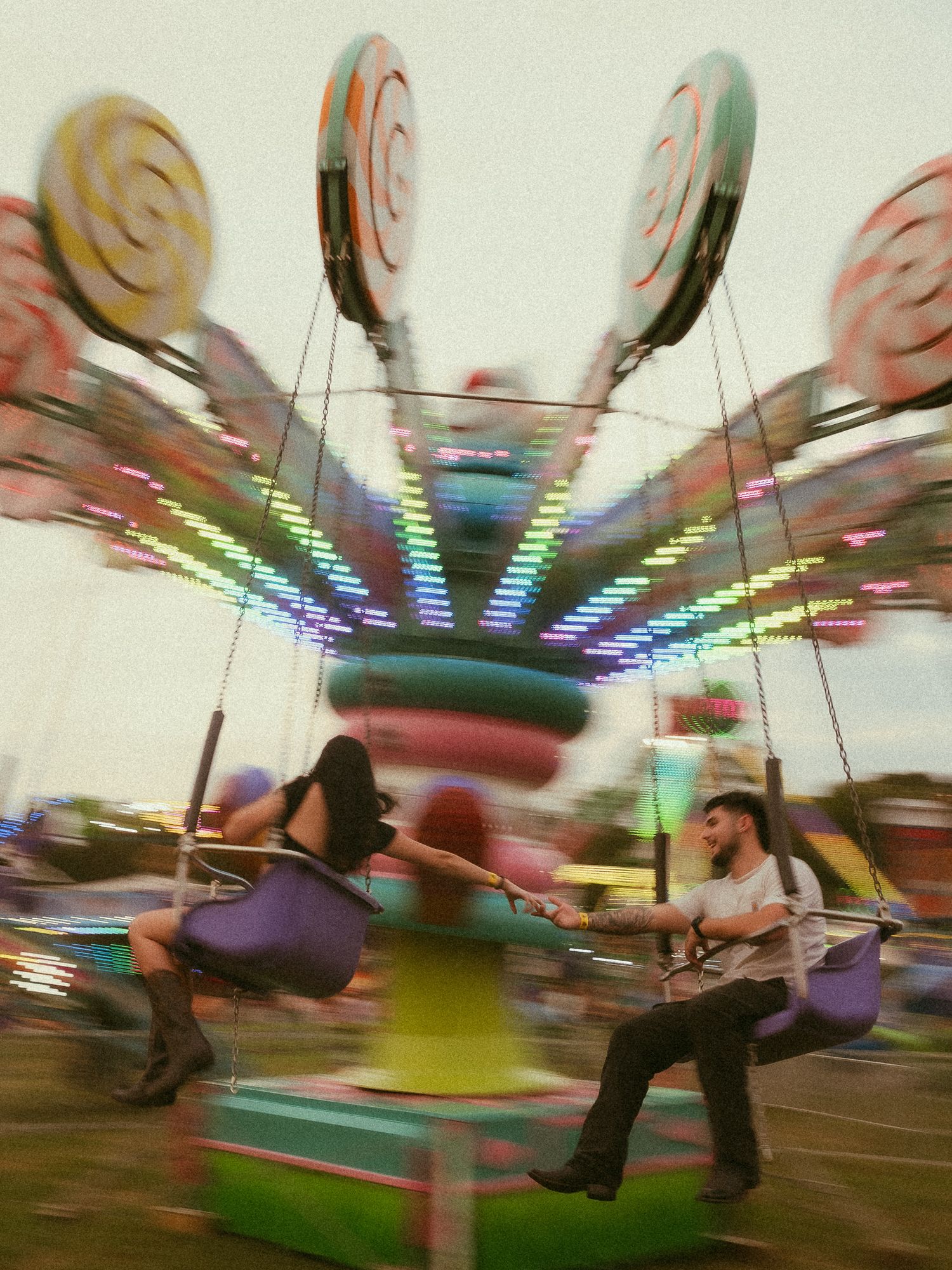 Couple riding colorful swing carousel at a carnival fair at night with motion blur lights.