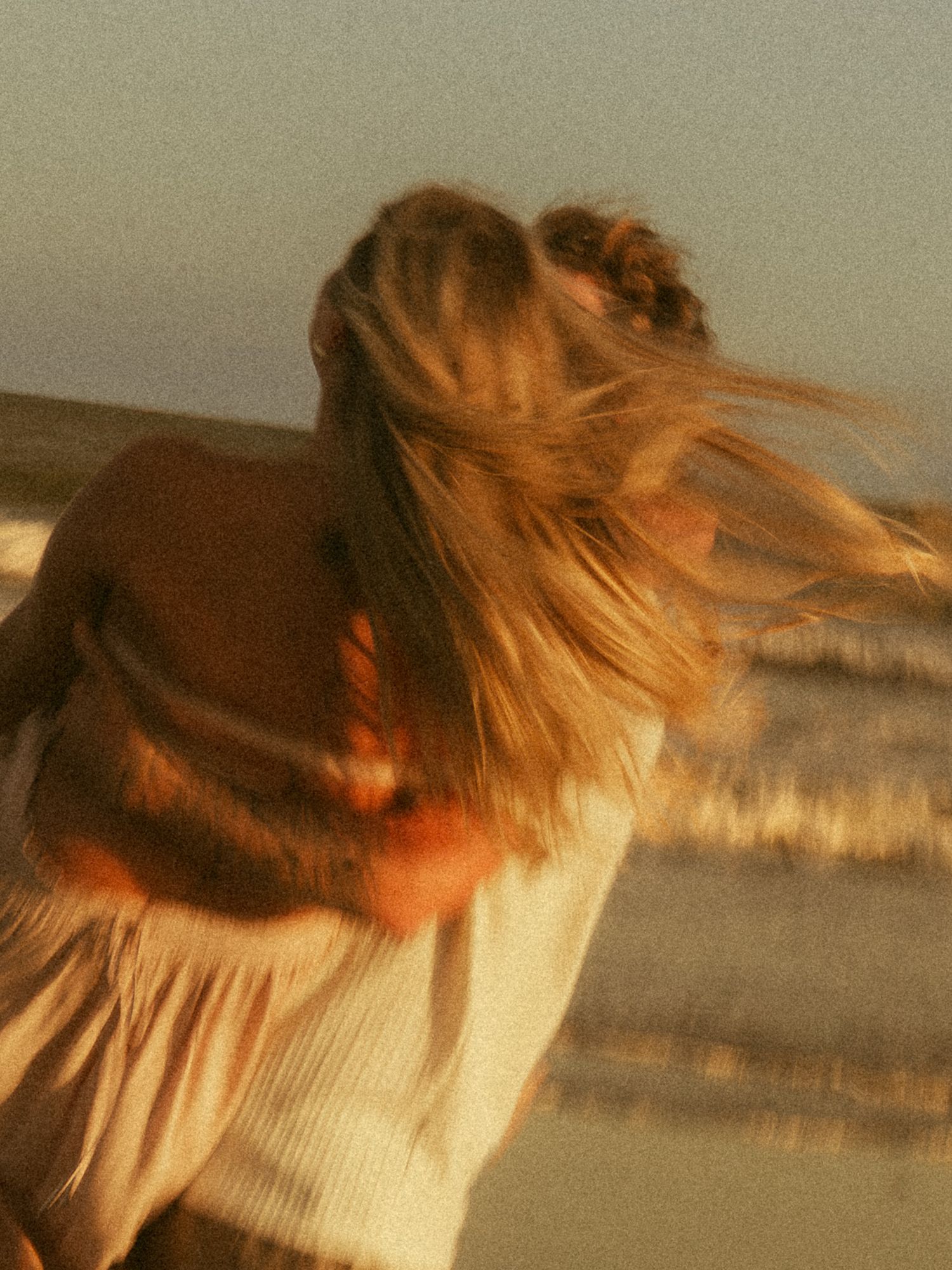 Blurred motion of a woman with flowing blonde hair on a windy beach at golden hour.