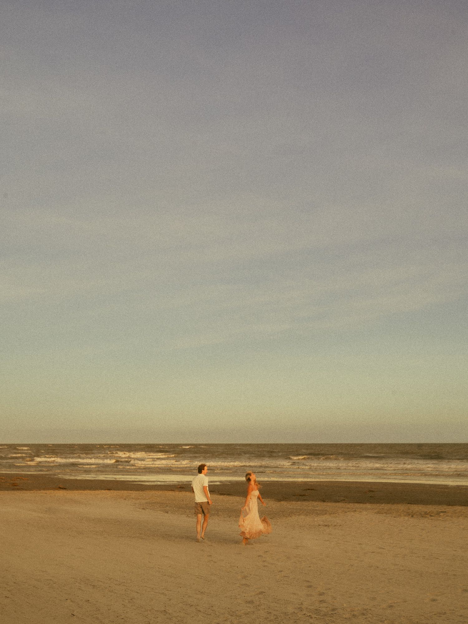 Couple walking hand in hand on a vast sandy beach at golden hour by the ocean.