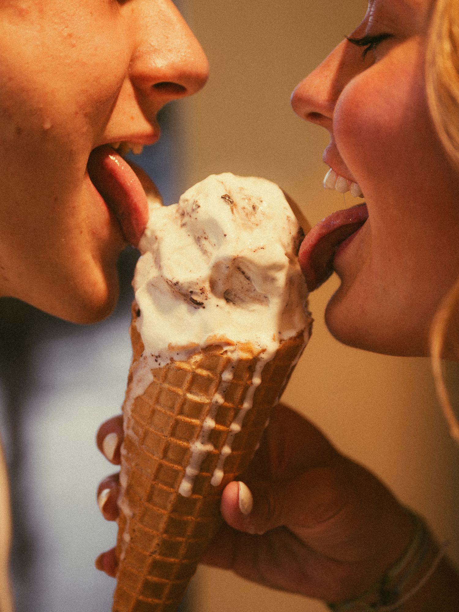 Two people sharing a scoop of ice cream on a waffle cone, each licking from opposite sides.