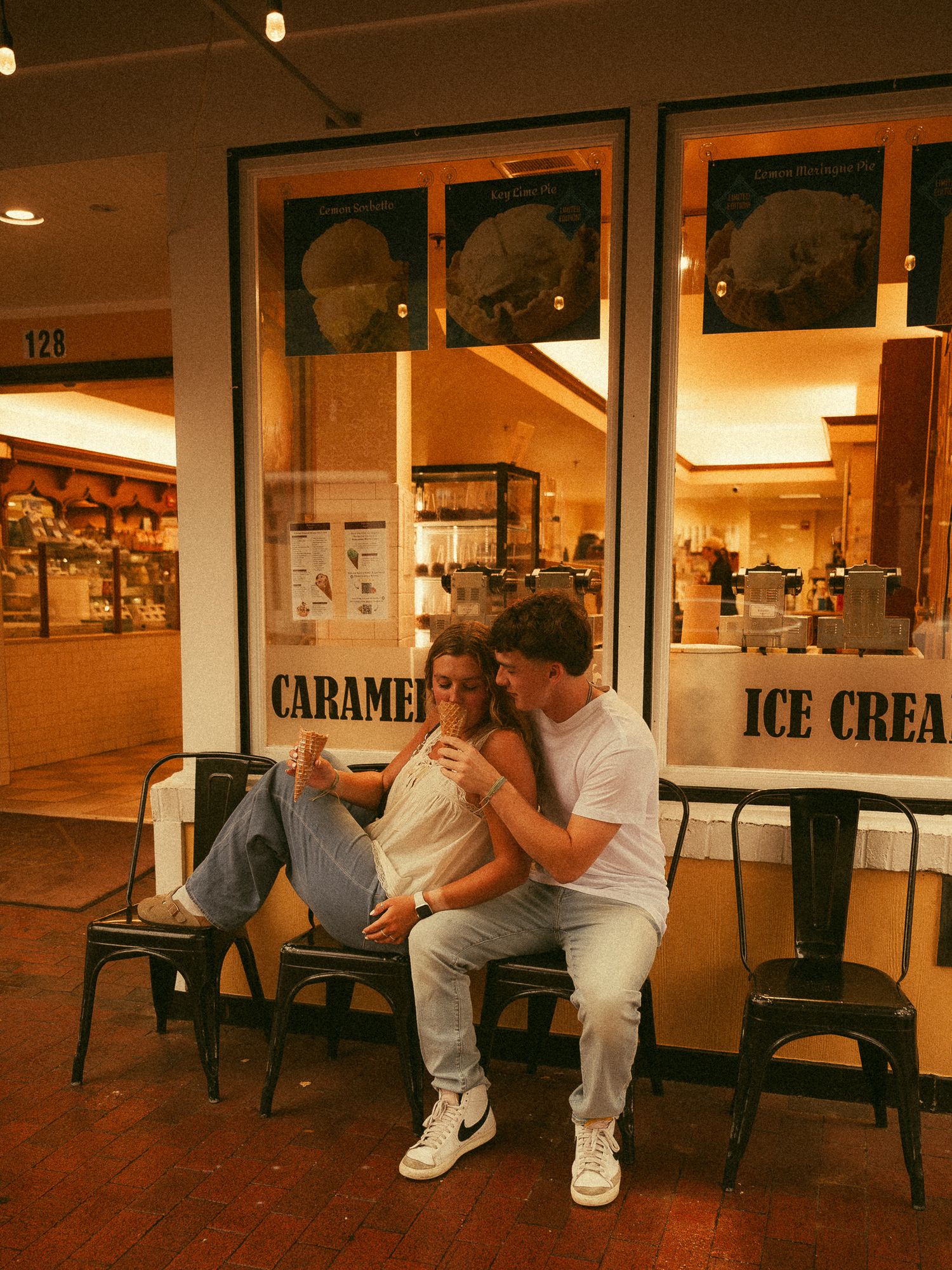 Couple sitting together on bench outside an ice cream and caramel shop at night.