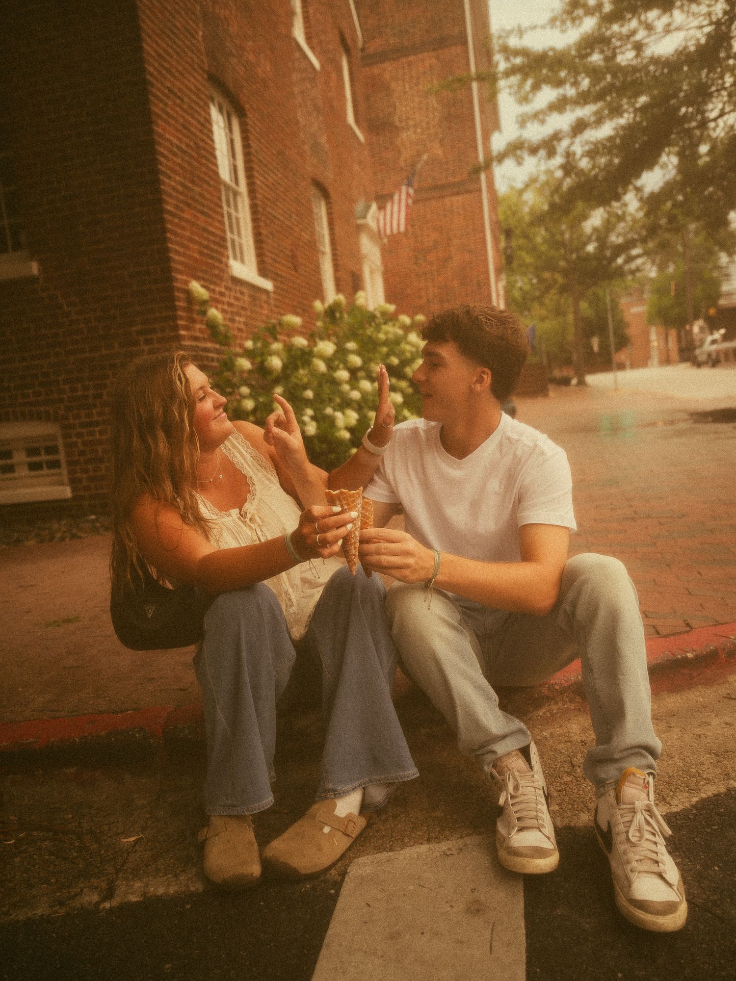 Young couple sitting on a curb sharing an ice cream cone on a warm summer day.