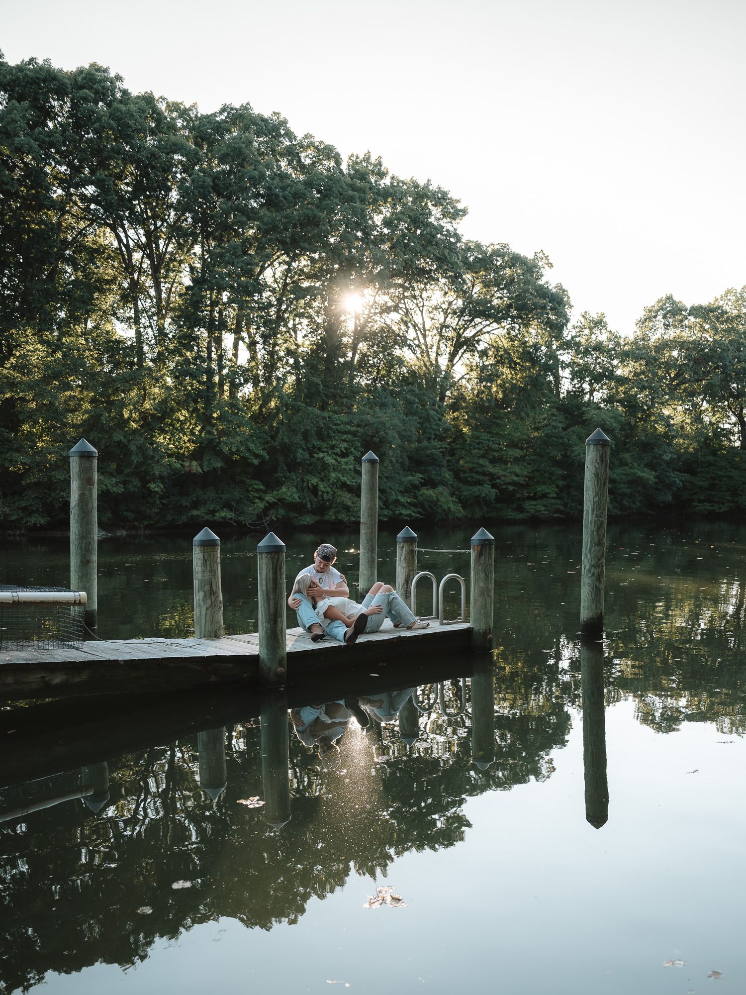 A peaceful dock extends over calm reflective waters at sunset with trees silhouetted in the background.